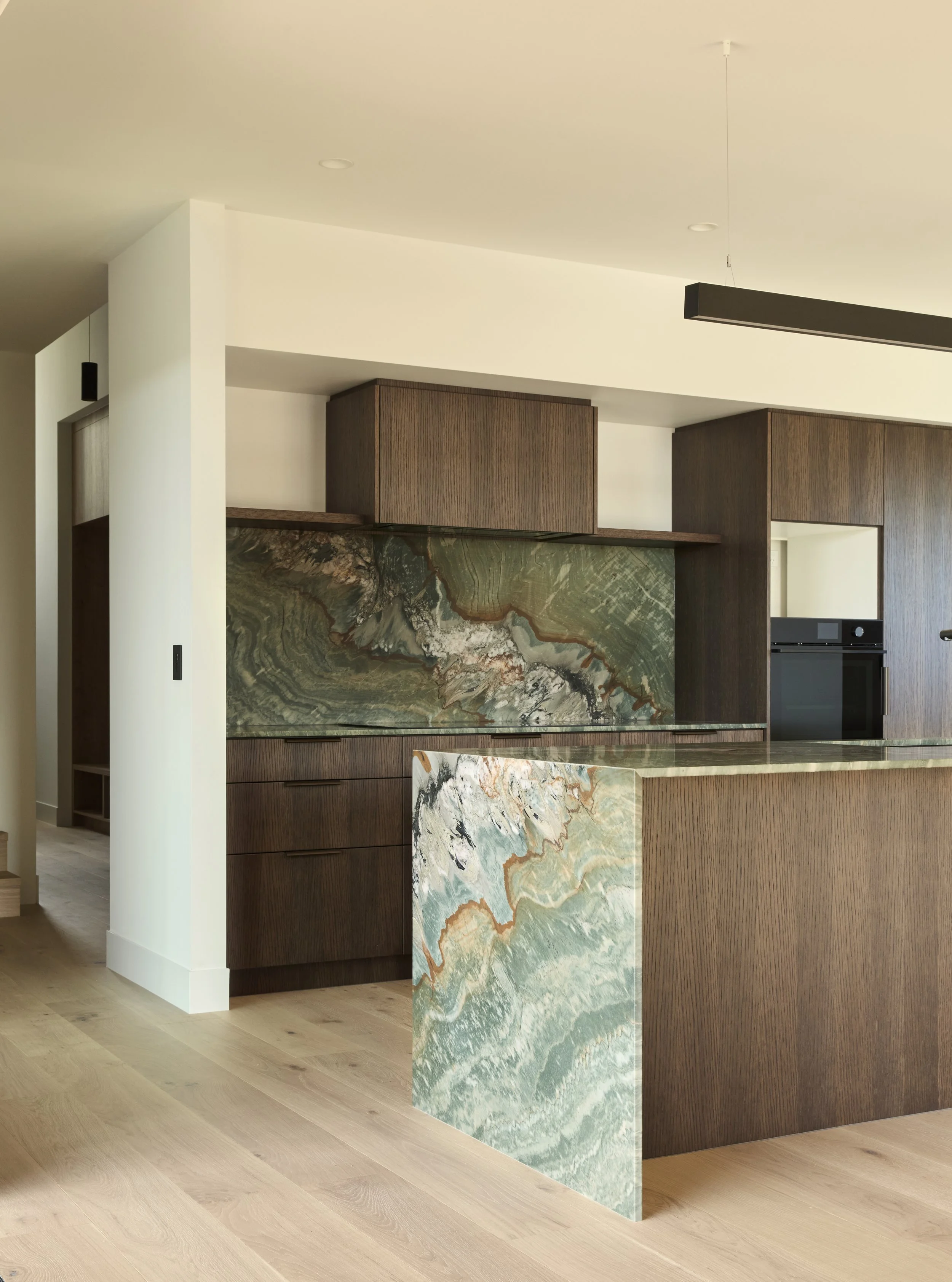 Modern kitchen with wooden cabinetry, marble countertops, and a decorative marble backsplash with swirl patterns of green, beige, and brown built on Waiheke Island.