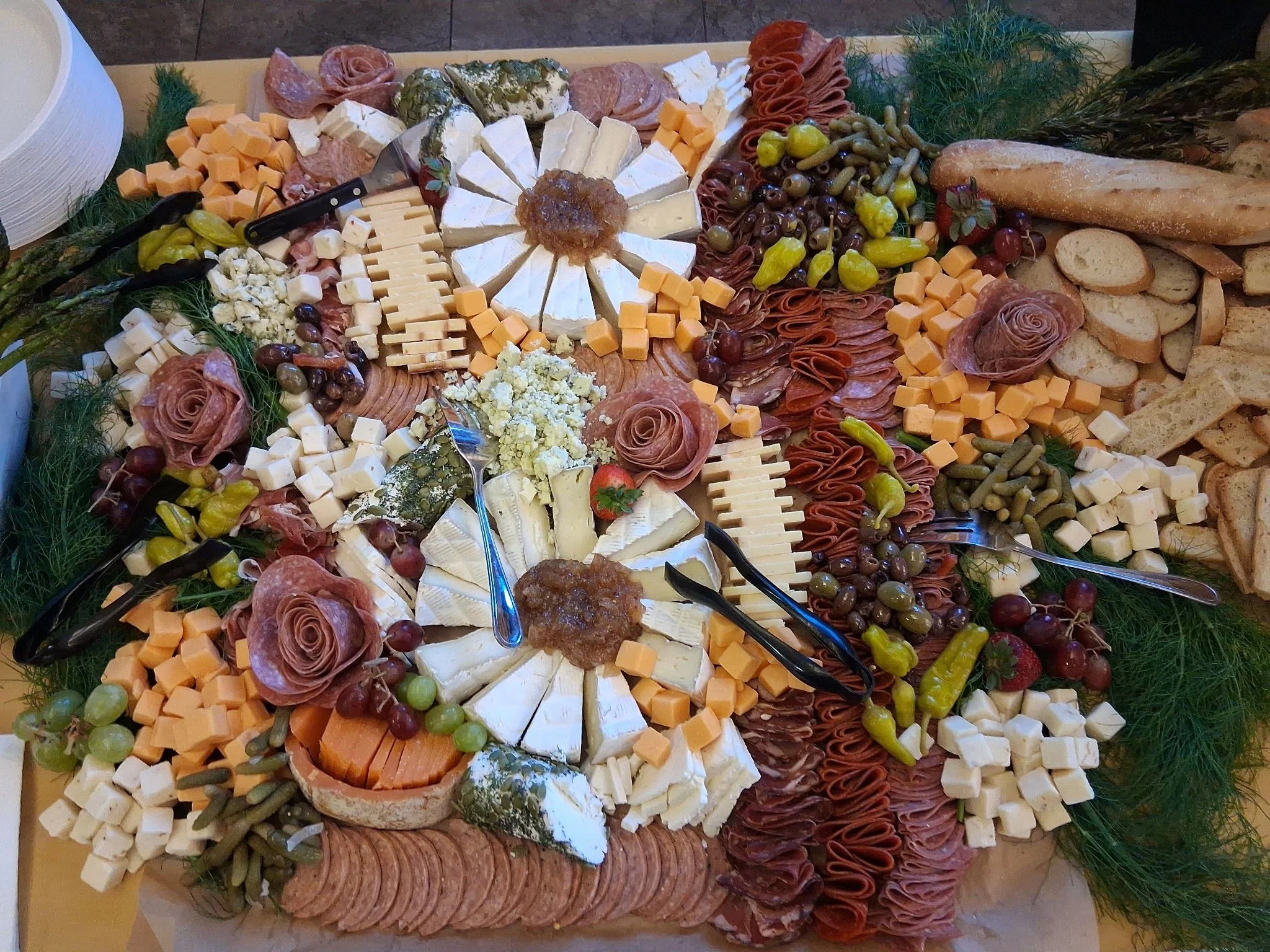 A cheese and charcuterie platter with various cheeses, cured meats, grapes, crackers, bread, and garnishes.
