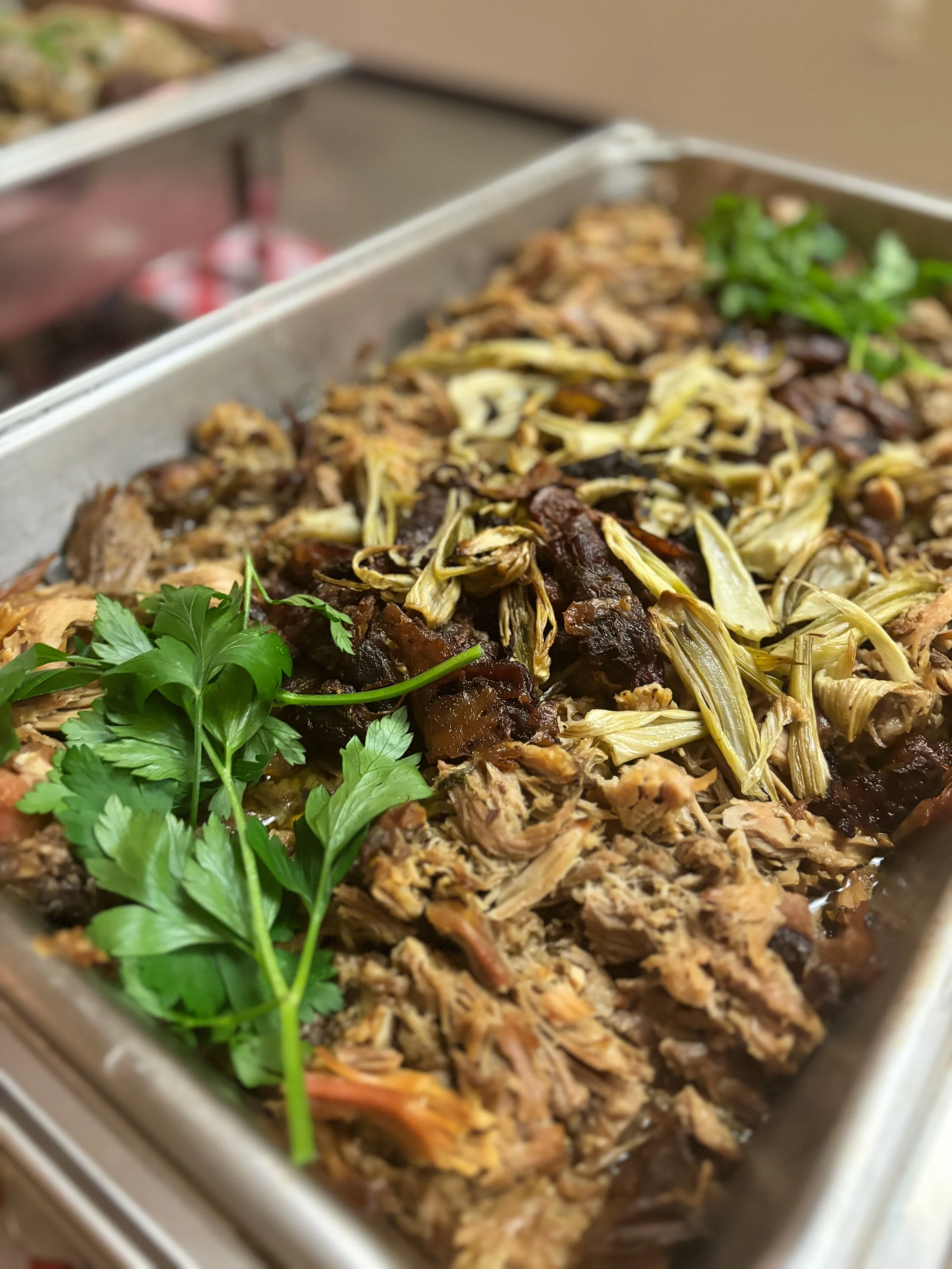 A tray of cooked shredded braised pork garnished with fresh parsley and topped with shredded vegetables.