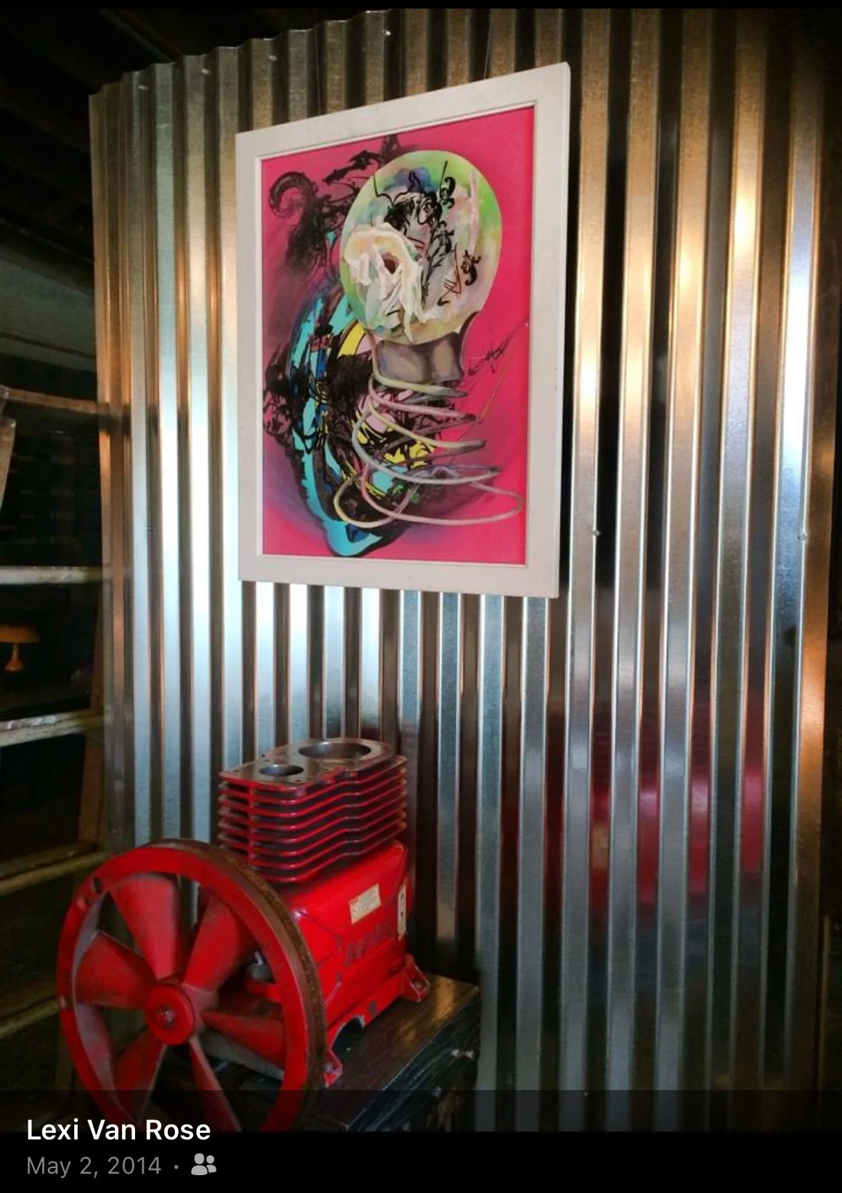Colorful abstract artwork on a silver corrugated metal wall, with a red vintage engine or air compressor at the bottom.