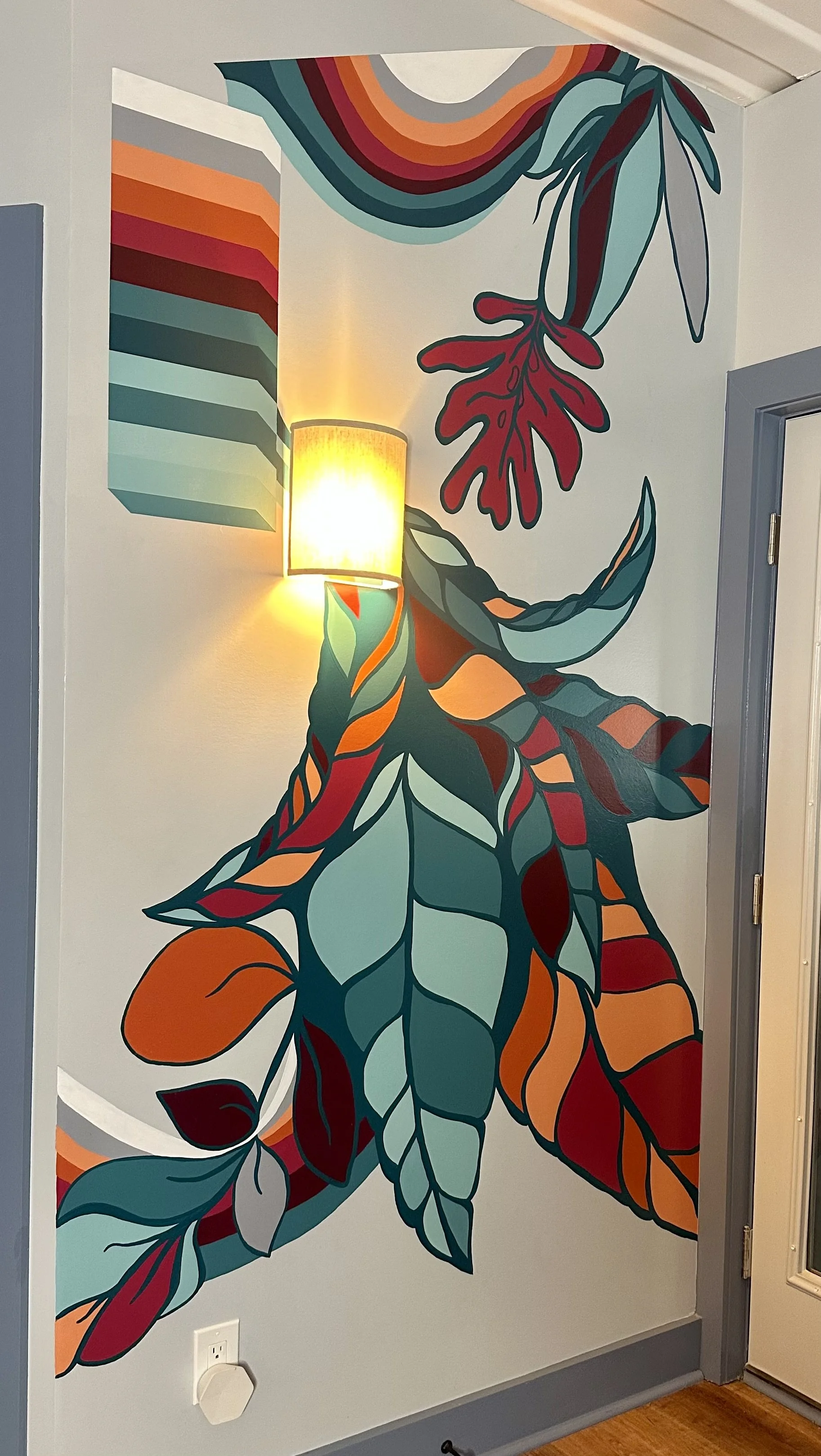 Colorful wall mural of leaves and abstract shapes, illuminated by a wall-mounted lamp.