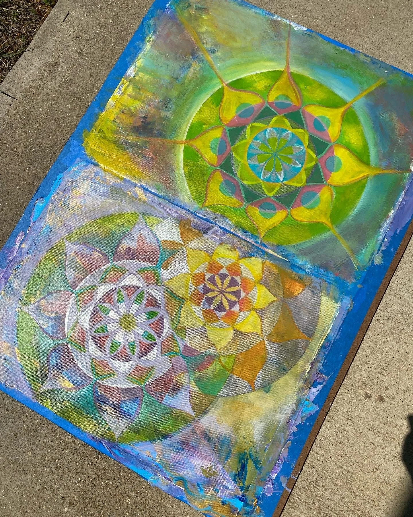 Two colorful abstract mandala paintings on fabric laid on a sidewalk.