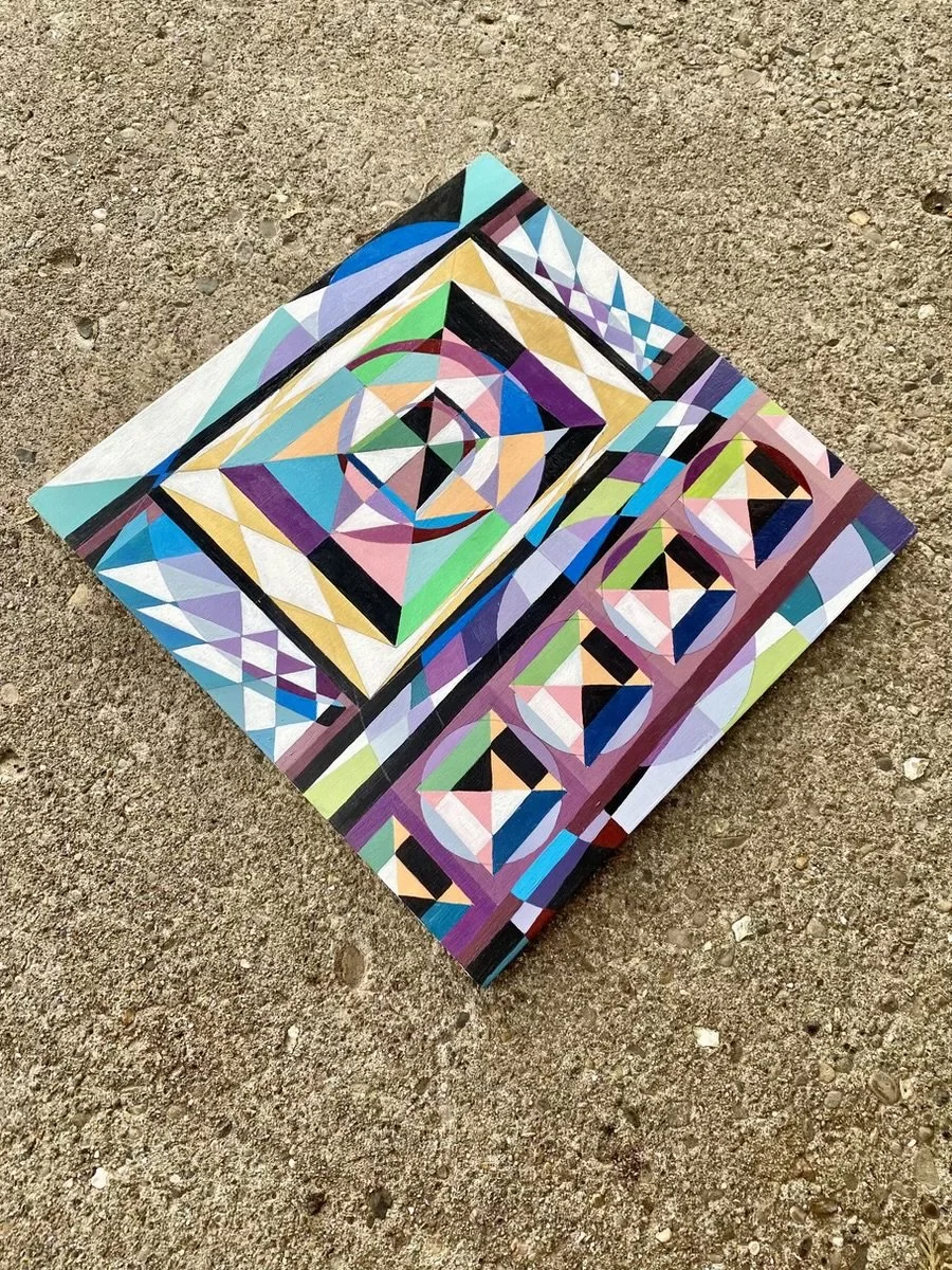 Colorful geometric abstract painting on canvas lies on dirt ground.