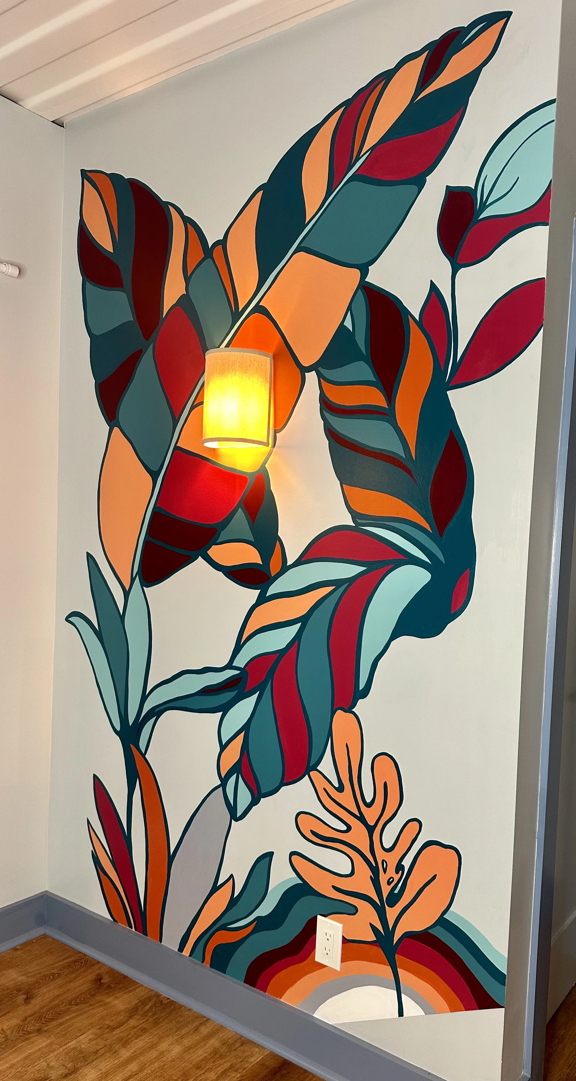 Colorful mural of abstract leaves and foliage on wall, with a wall-mounted yellow light fixture and electrical outlet at the bottom.