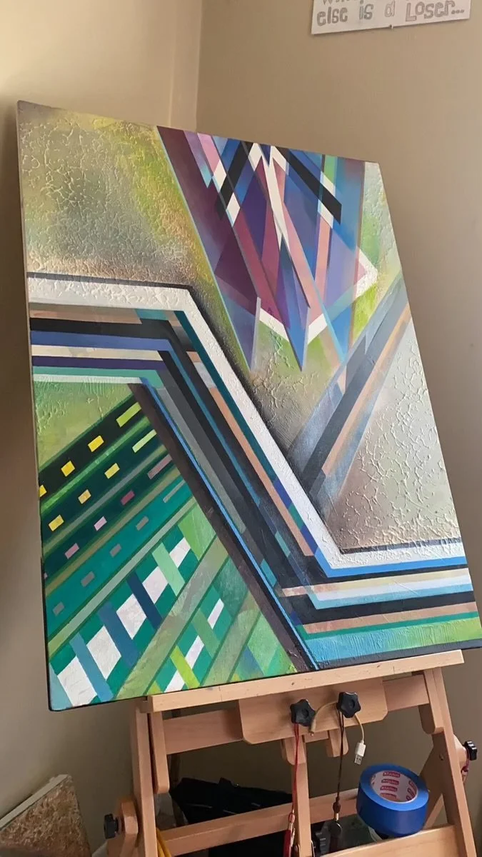 Abstract geometric painting with vibrant colors, including blues, greens, pinks, and purples, on a canvas resting on an easel.