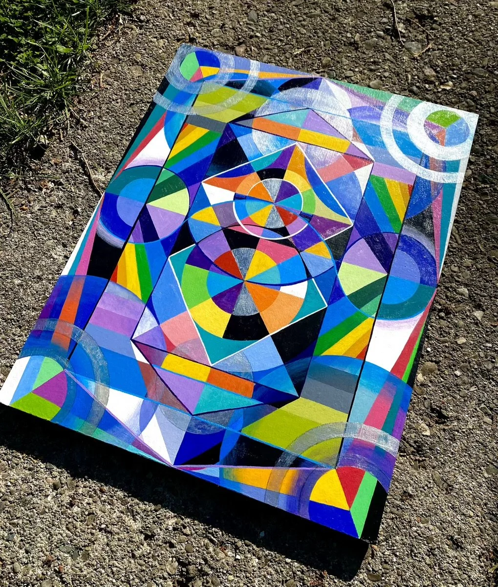 Colorful geometric abstract painting on a flat surface outdoors on dirt ground.