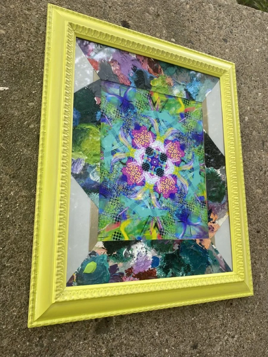 Colorful abstract artwork with vibrant colors and intricate patterns, framed in a bright yellow ornate frame, placed on a concrete surface.