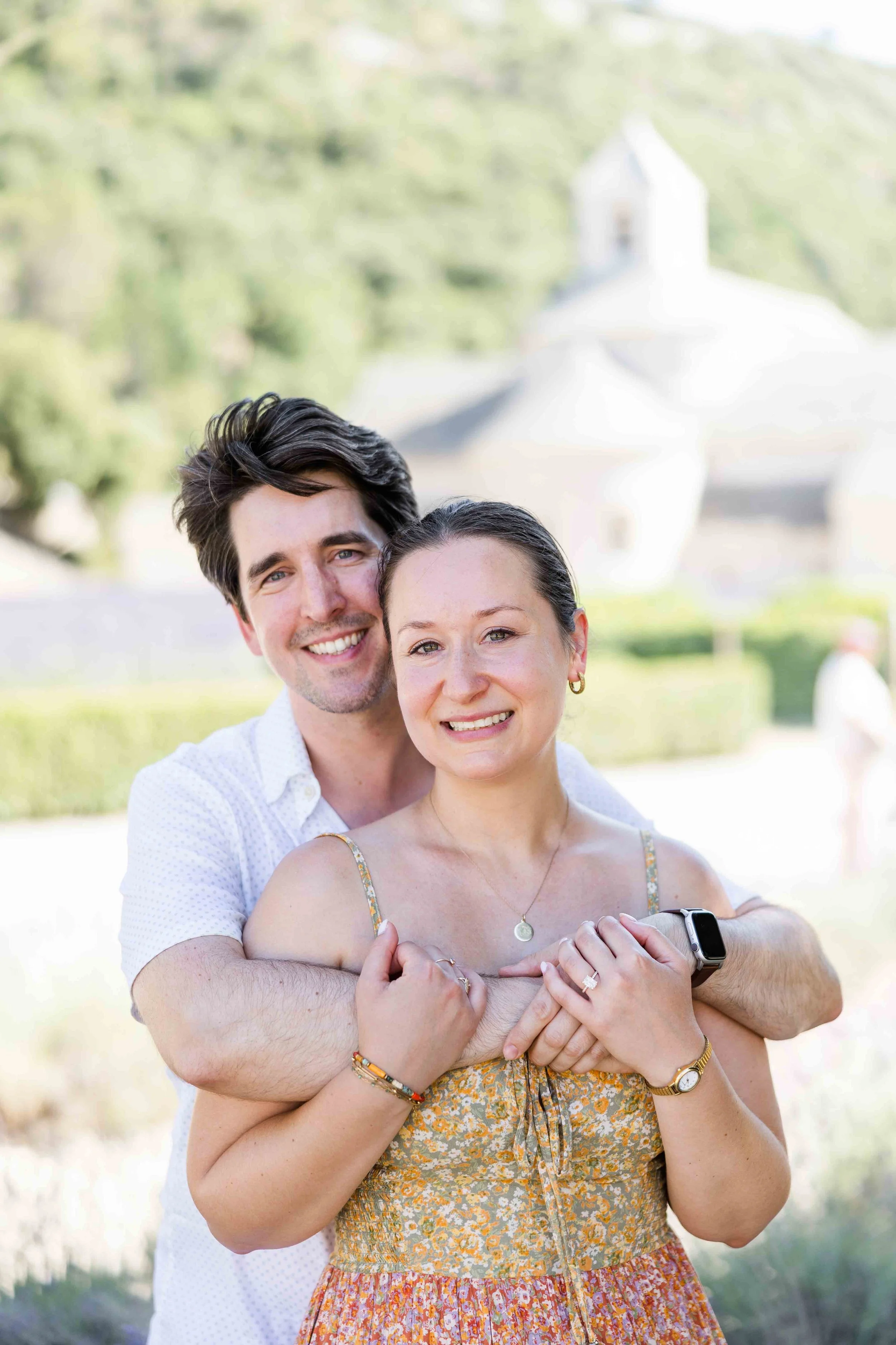 Newly engaged couple smiling and embracing with the lavender fields of Abbaye de Sénanque in the background