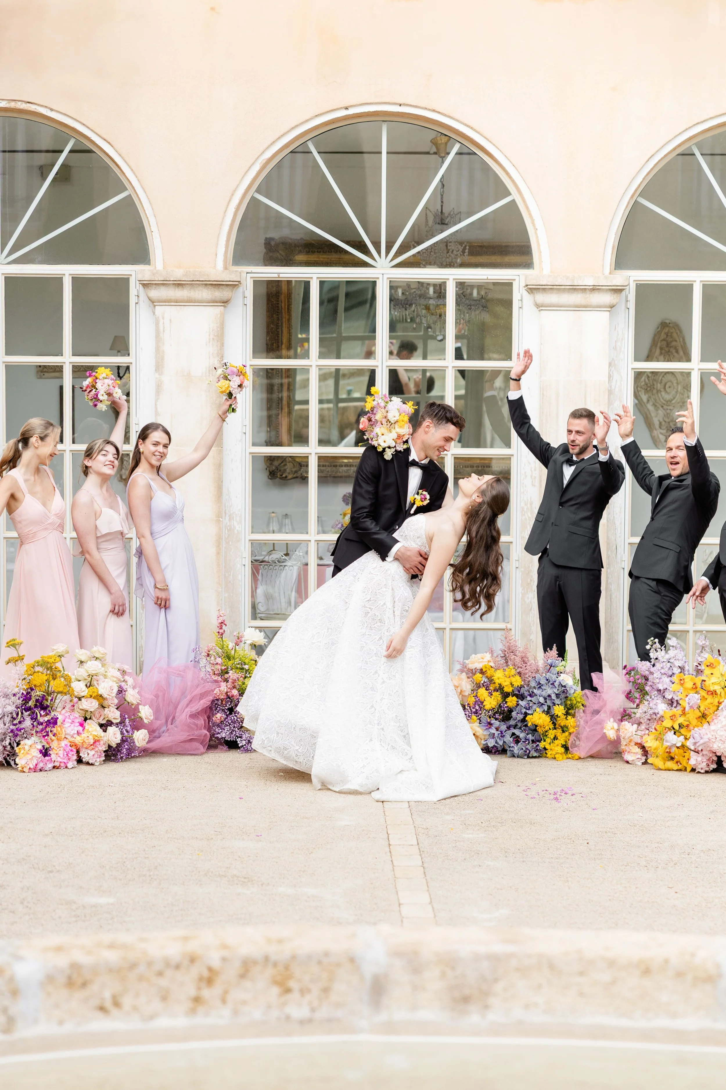 Wedding exit moment in front of a French estate with guests celebrating, flowers, and joyful confetti atmosphere.