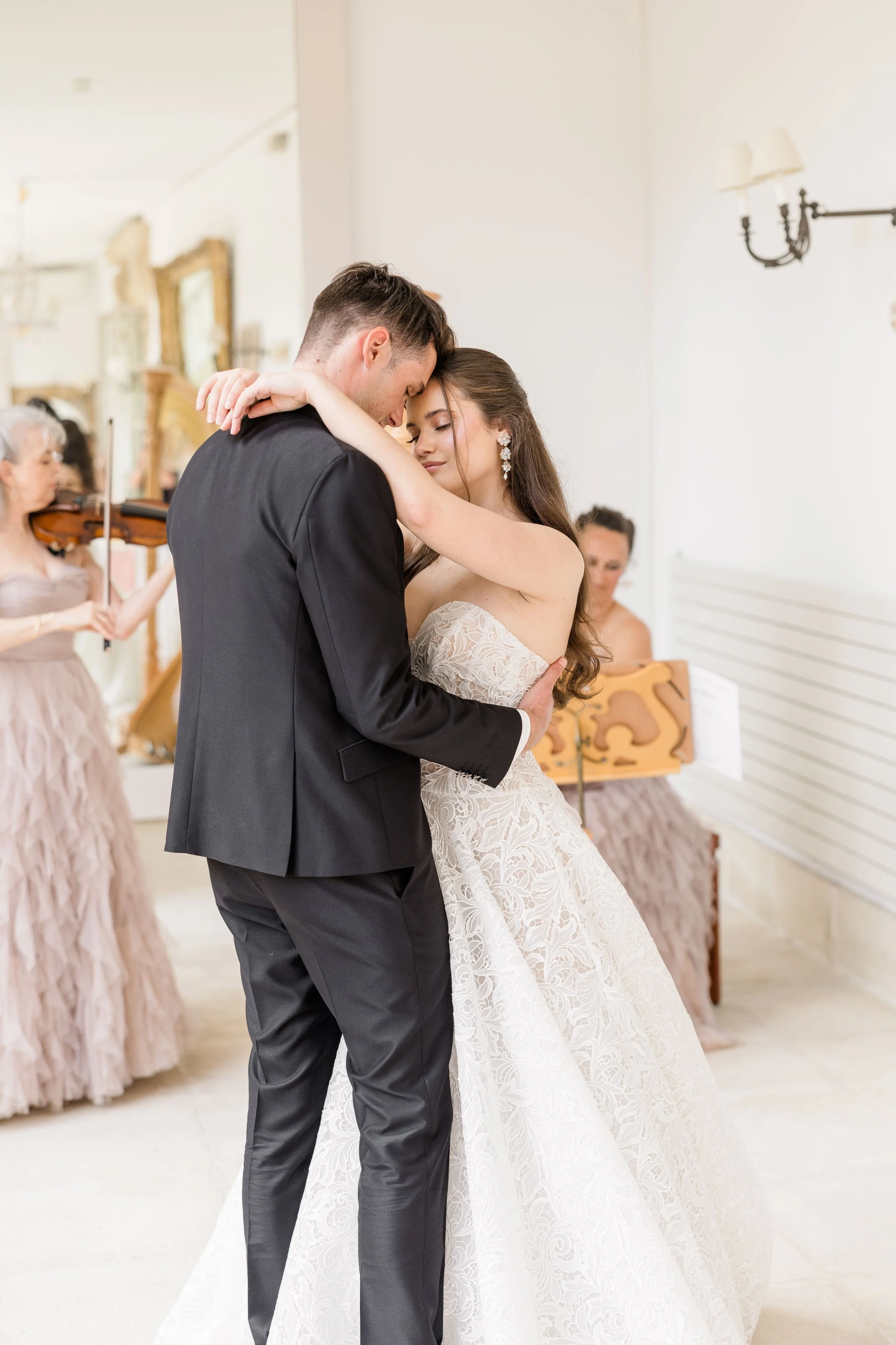 Romantic indoor wedding moment of a bride and groom embracing during an elegant ceremony in a soft, light-filled Provence setting.