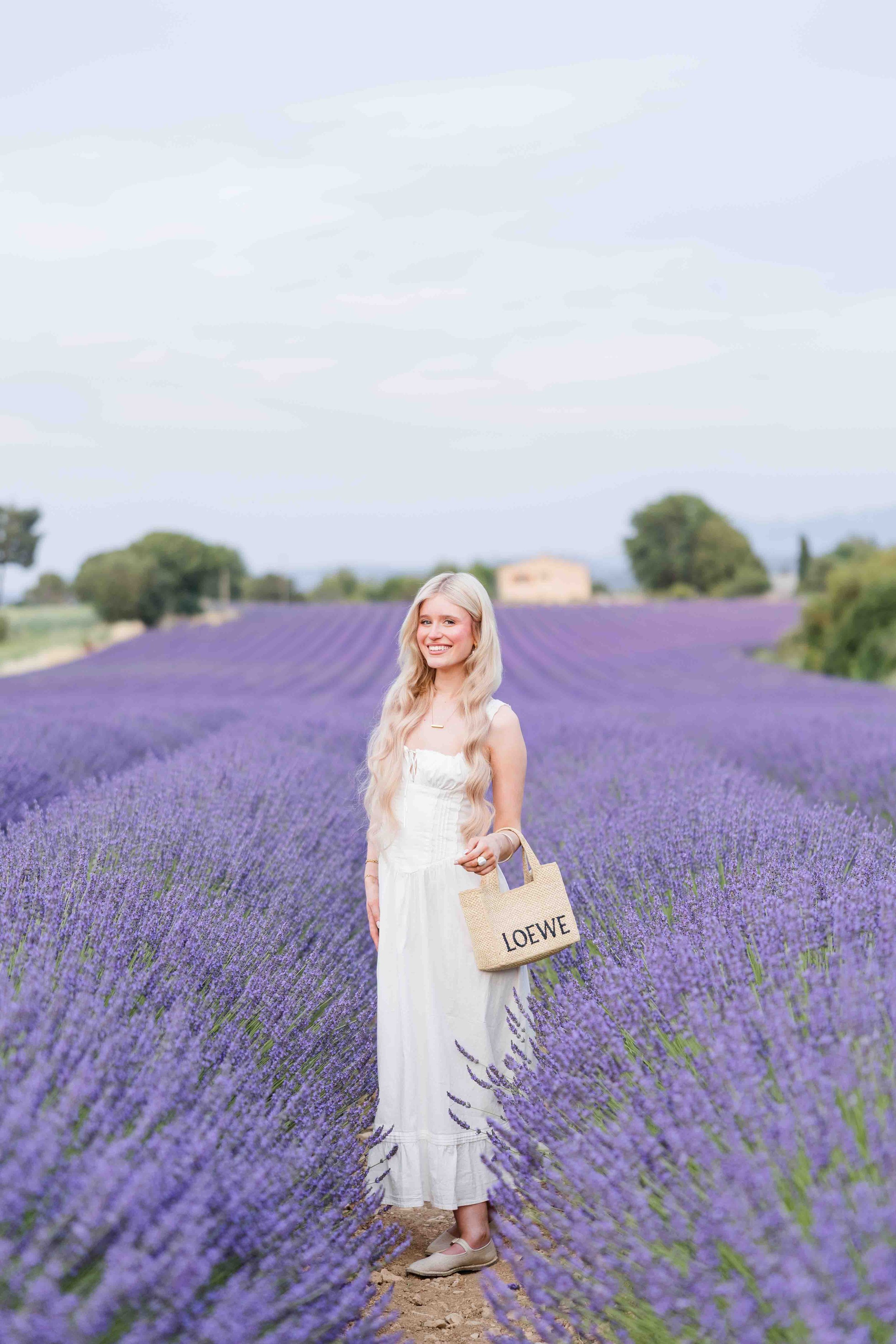  Woman walking through vibrant lavender rows during a summer photoshoot in Provence. 
