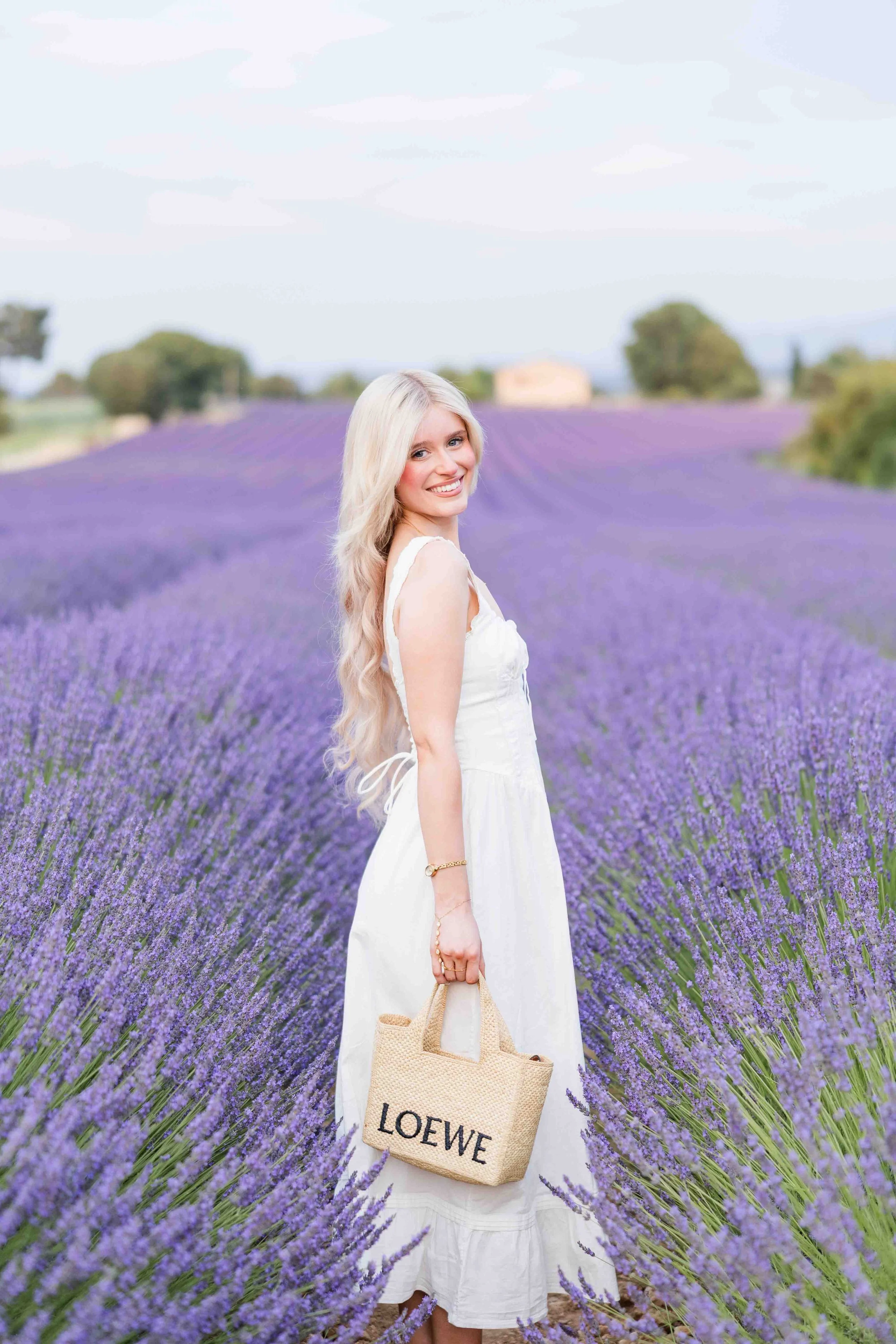  Side portrait of a woman in a white dress standing in lavender fields in Provence. 