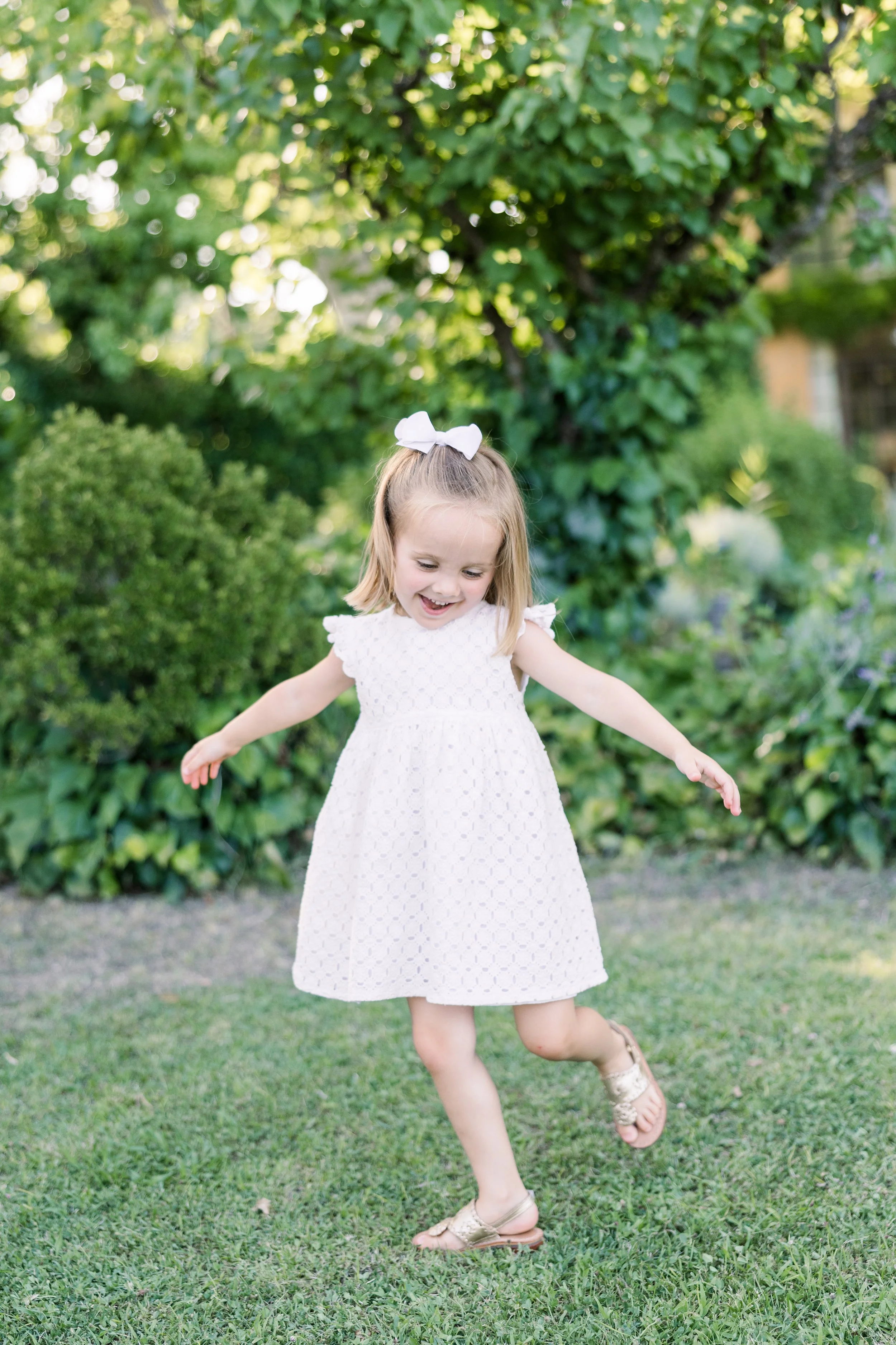 Young girl in white dress with arms raised playing outside in a Provence villa garden setting