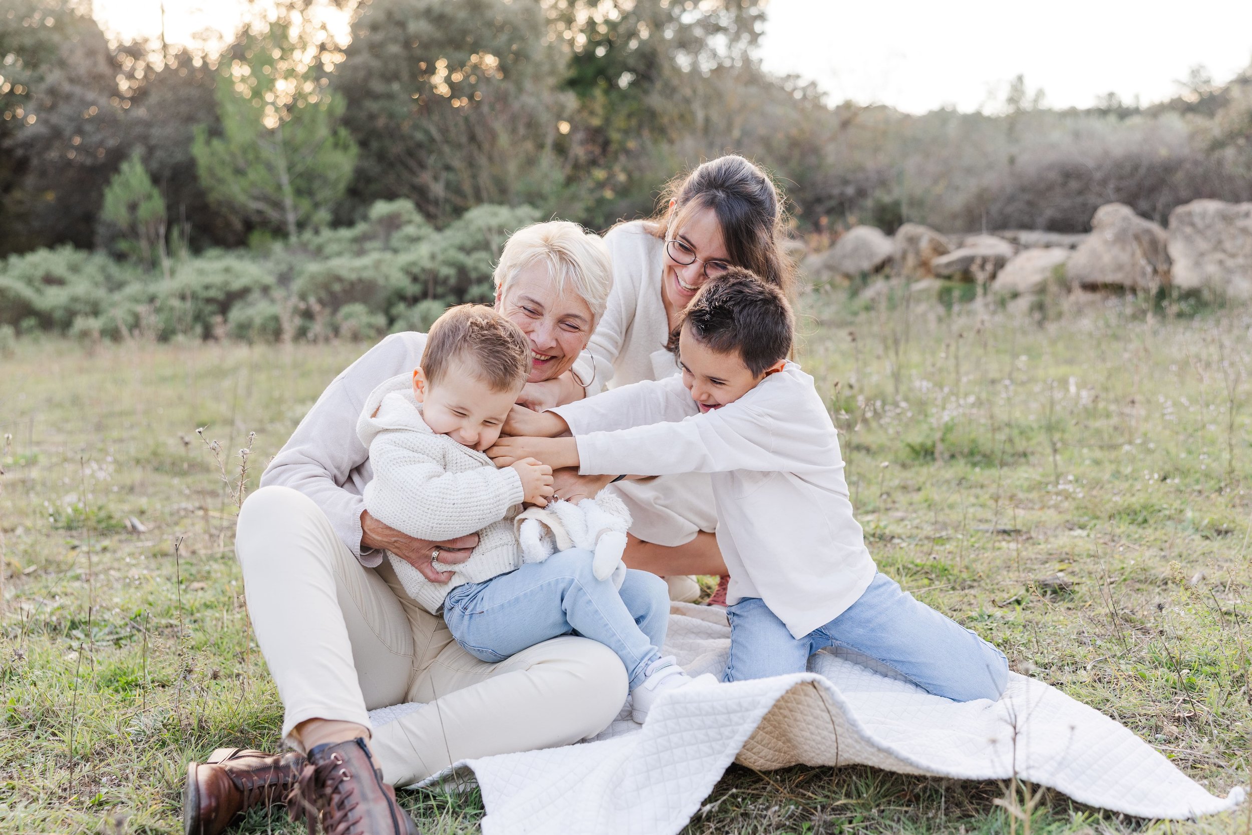 Family session in Provence with grandma the mom and 2 boys giggling and tickling each other surrounded by olive trees and stone