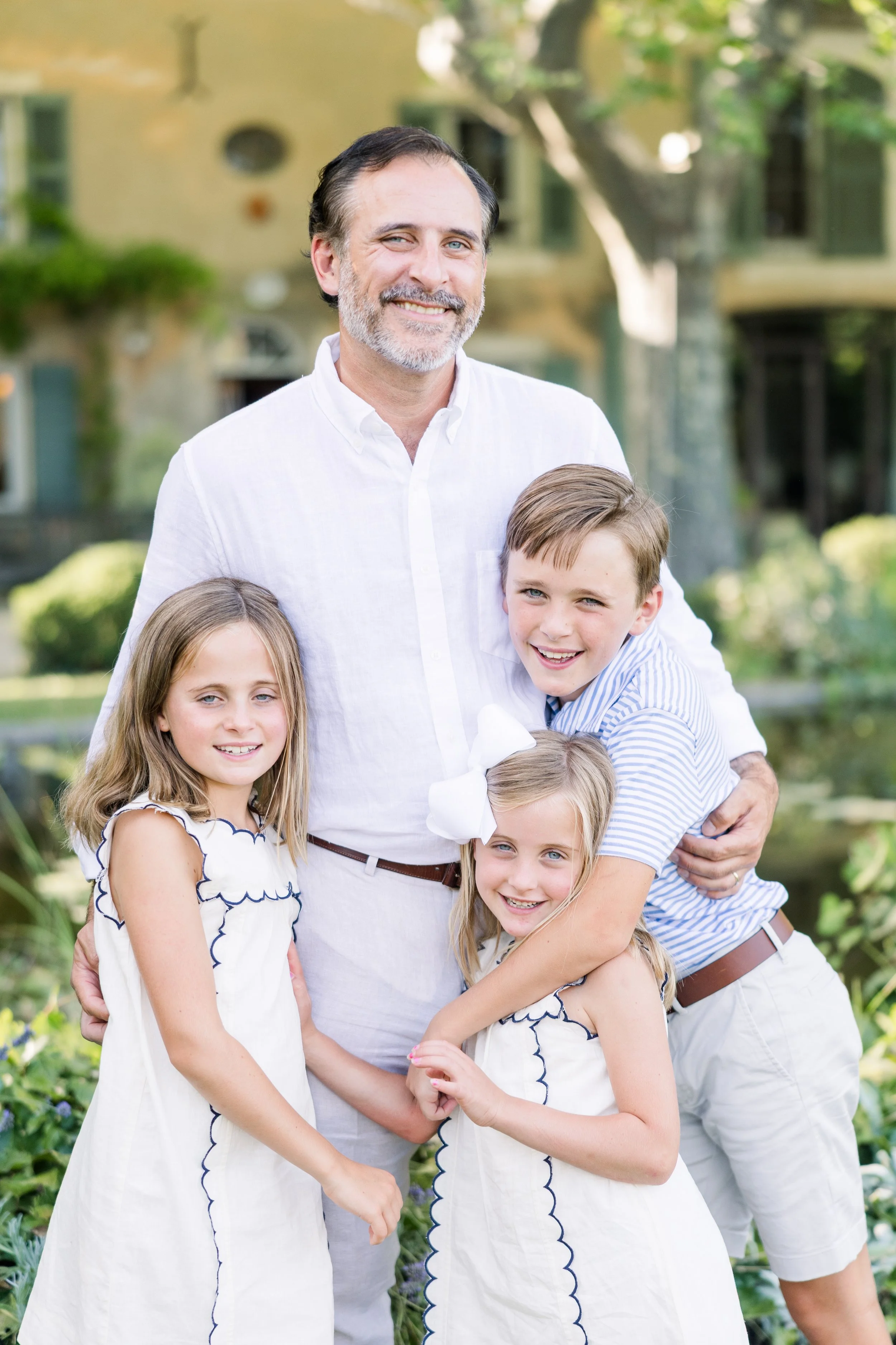 Dad with smiling daughter and son in casual family photo with Provence villa garden background
