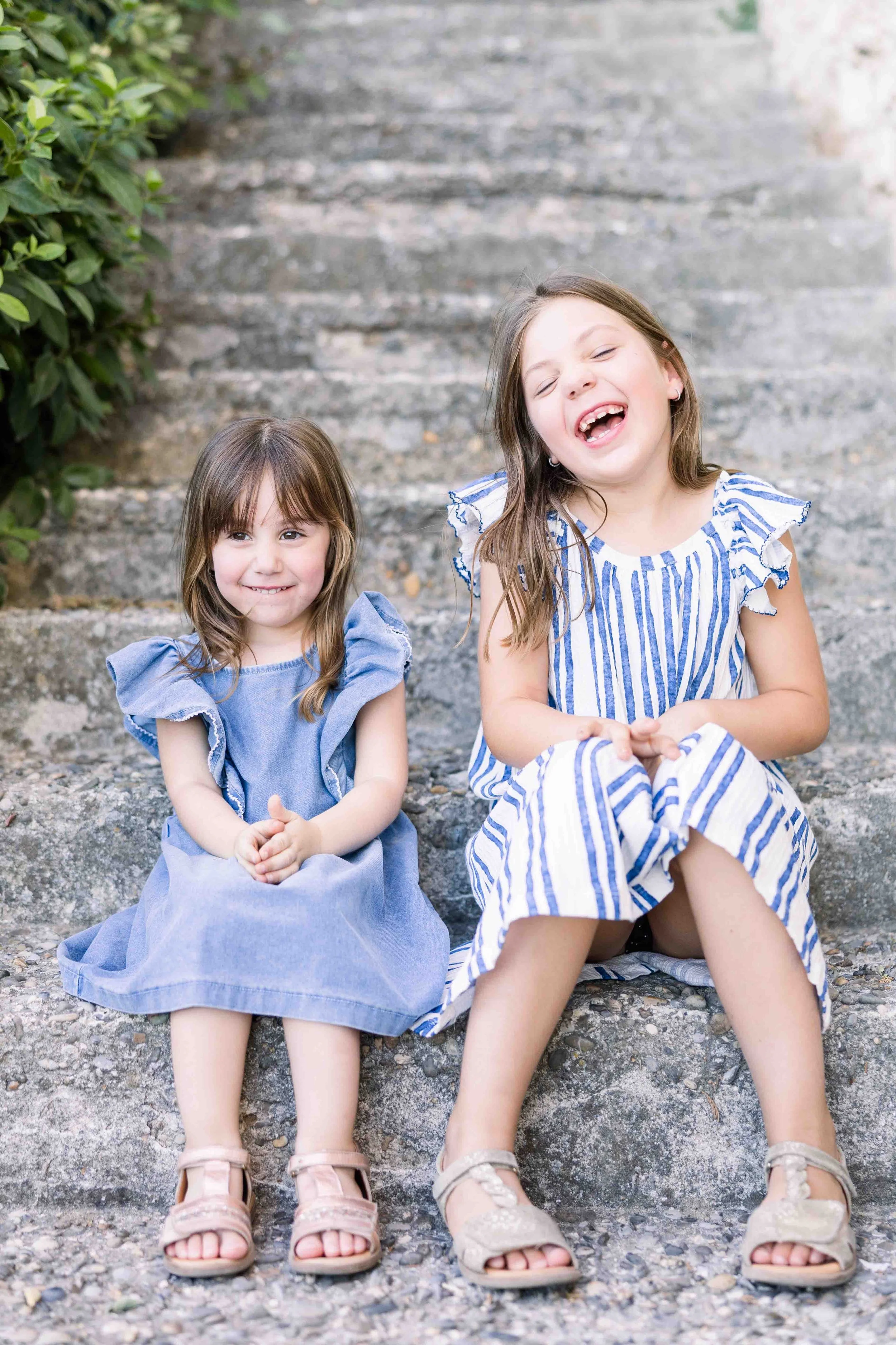 Two sisters sitting together on historic stone steps in a charming village in Provence.
