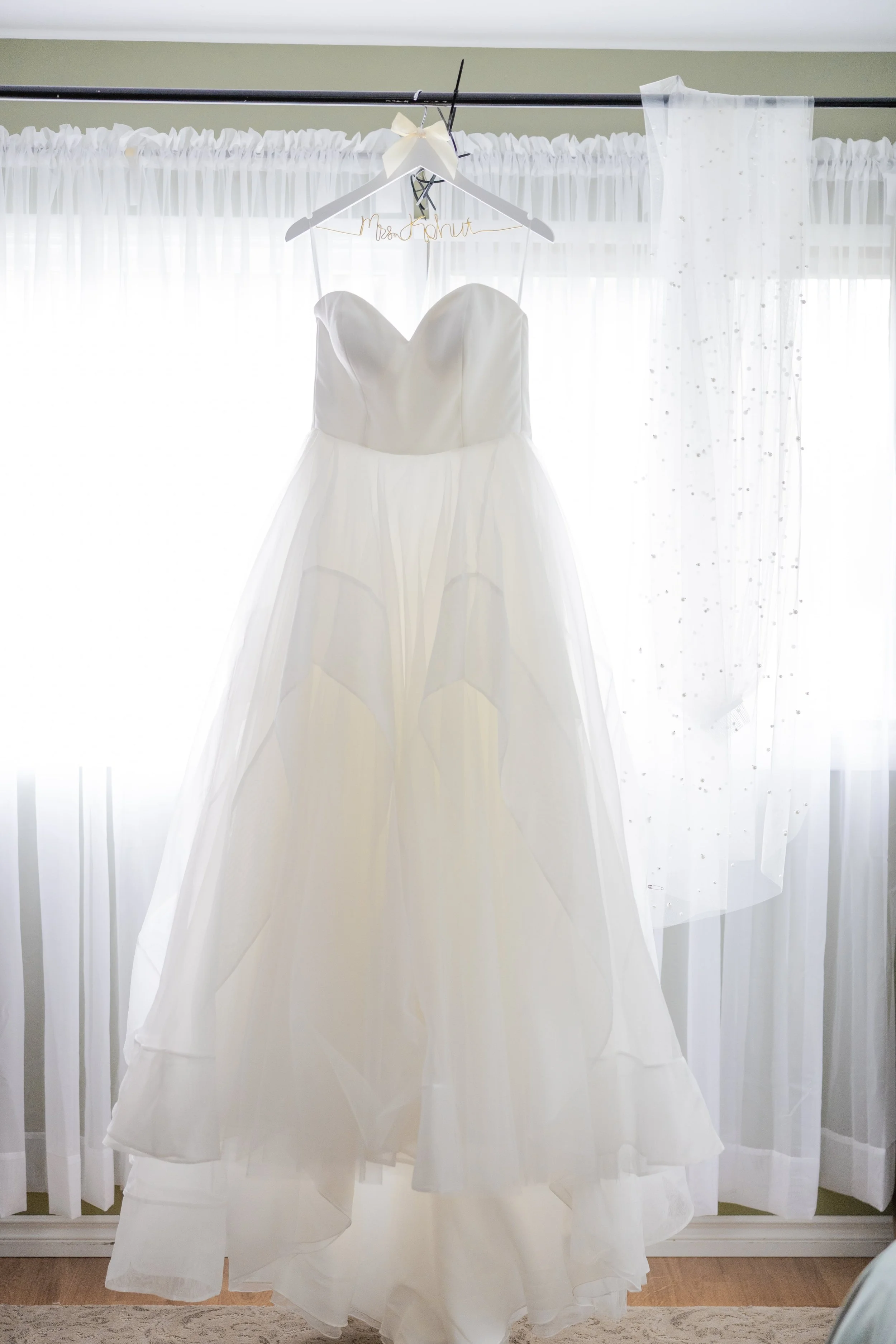 Elegant wedding dress hanging by the window with natural light