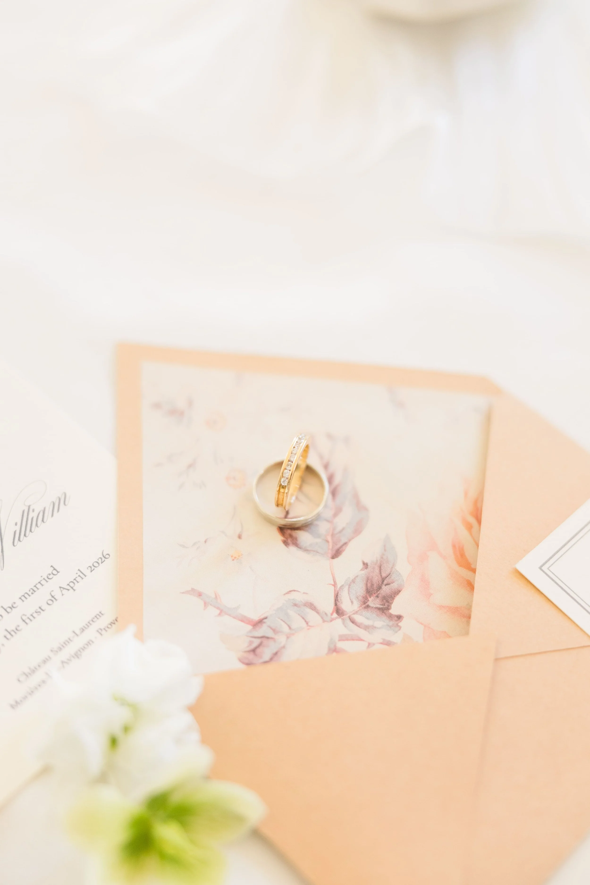 Bridal rings resting on romantic paper goods and invitation set