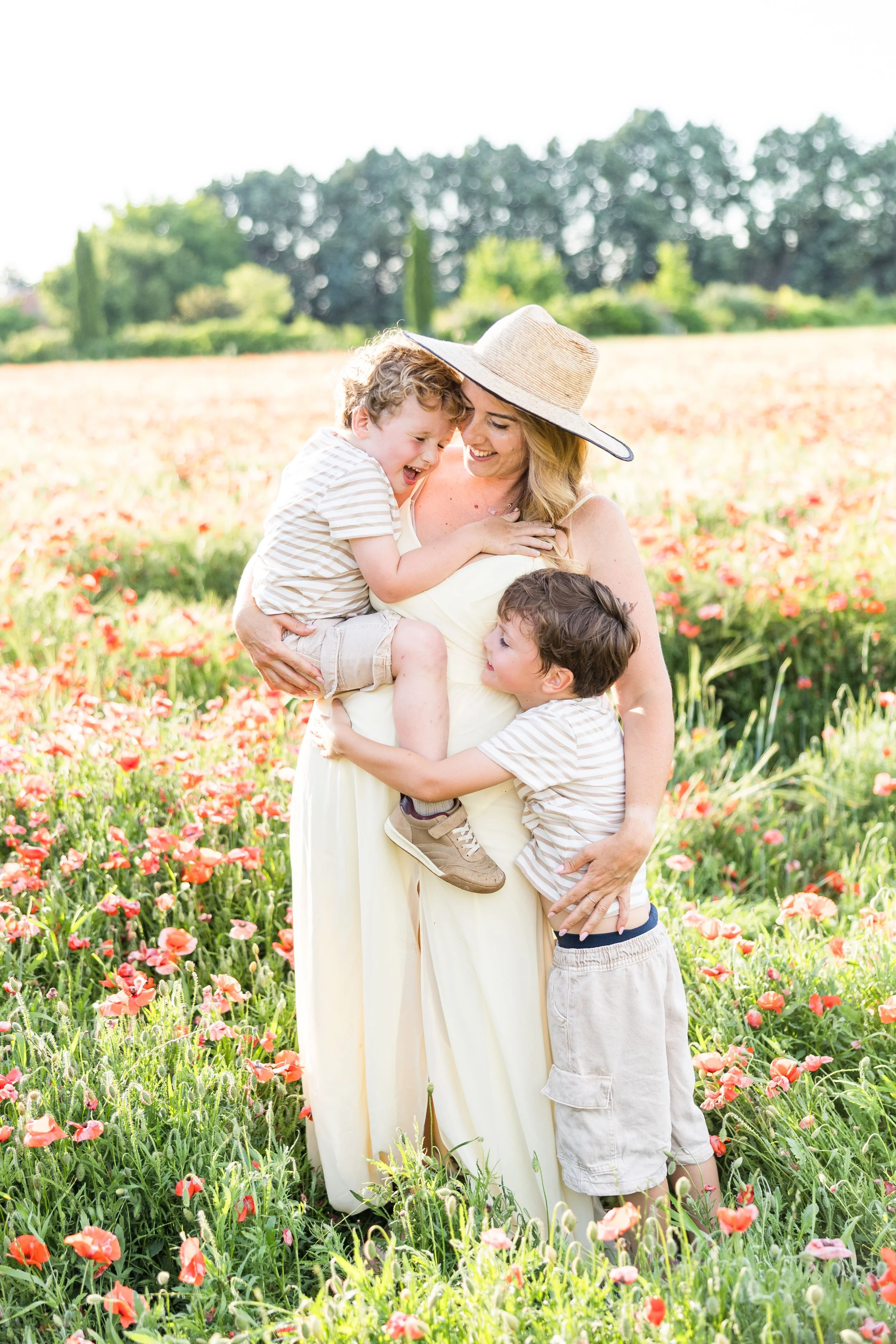 Mom holding her two boys in a puppy field in provence during golden hour everybody smiling and happy