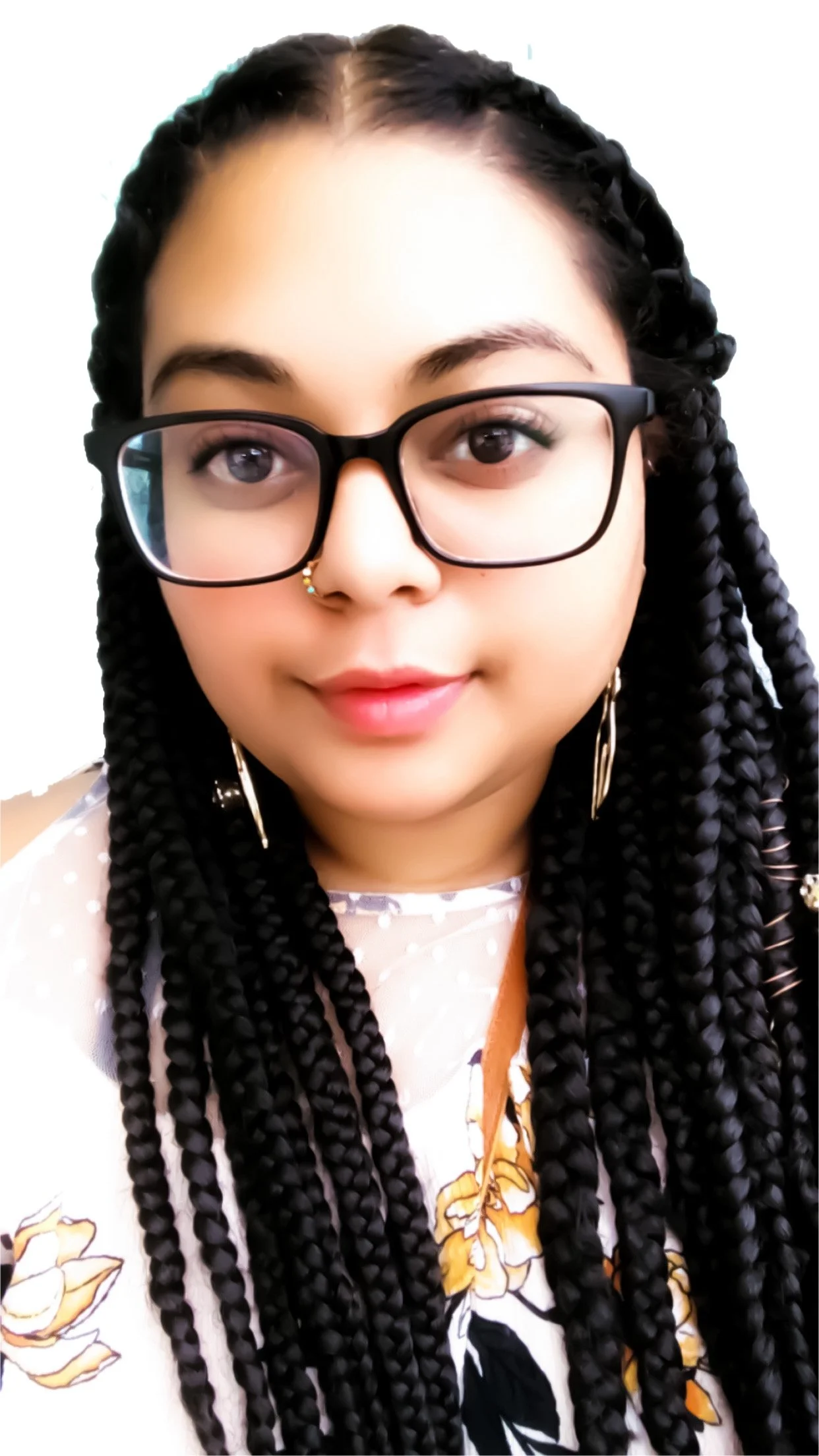 Close-up of a woman with long black braided hair, wearing black glasses, a nose ring, earrings, and a floral-patterned blouse with yellow and brown flowers.