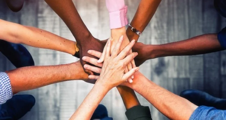 Group of diverse people placing their hands together in a show of teamwork and unity.