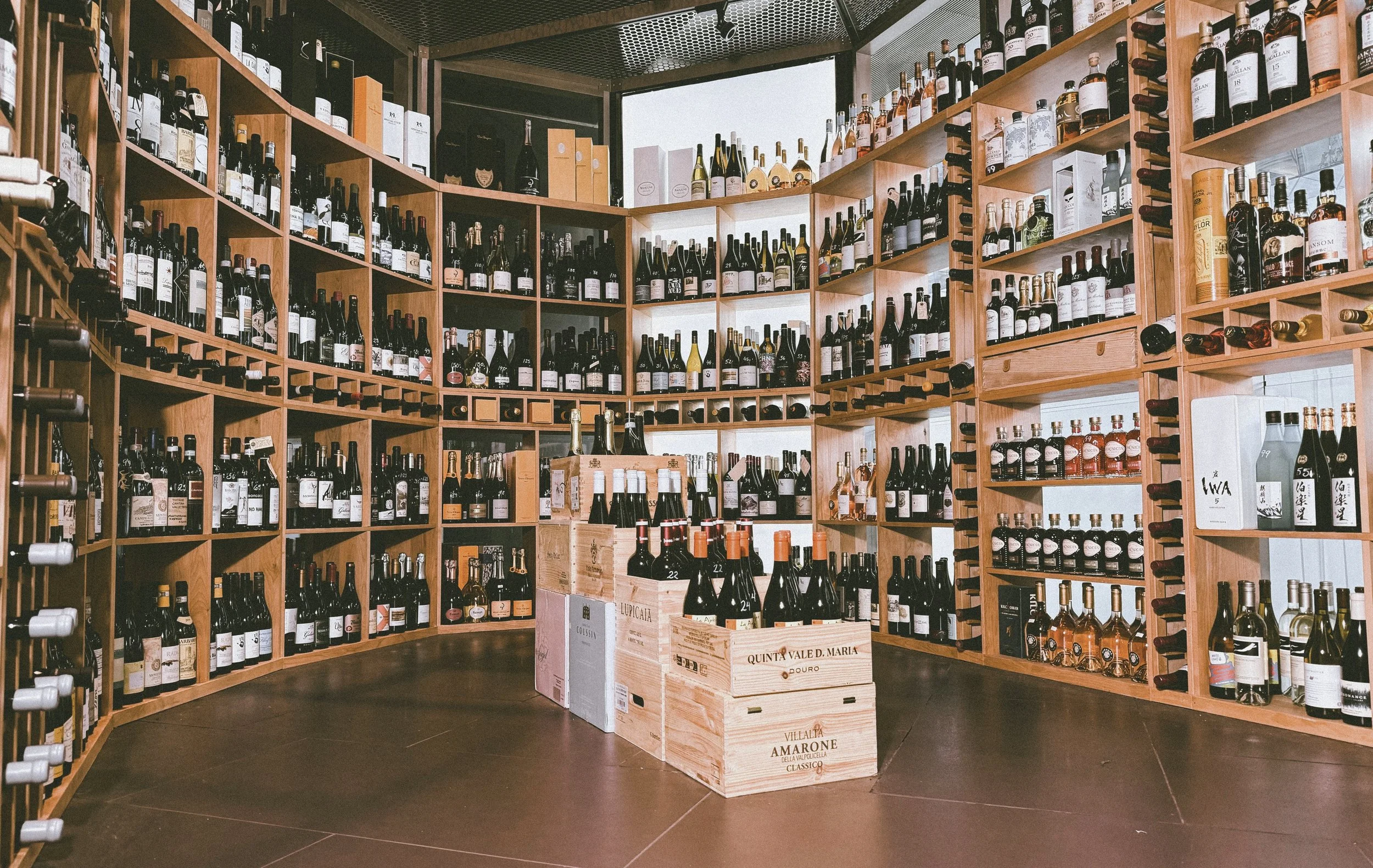 A circular wine cellar with wooden shelves filled with various bottles of wine, and cartons of wine bottles in the center.