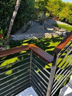 Restored exterior balcony wood railing with fresh finish overlooking a landscaped backyard
