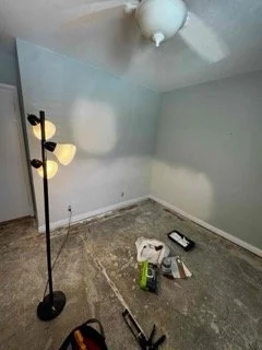 Room under renovation with exposed concrete subfloor showing sealed structural cracks and tools prepared for baseboard installation