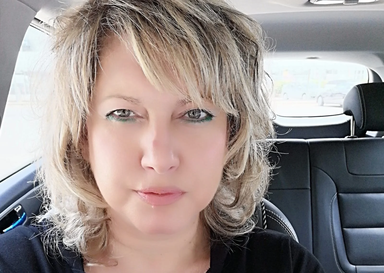 Close-up of a smiling woman with blonde hair, in a cozy car with leather seats setting.