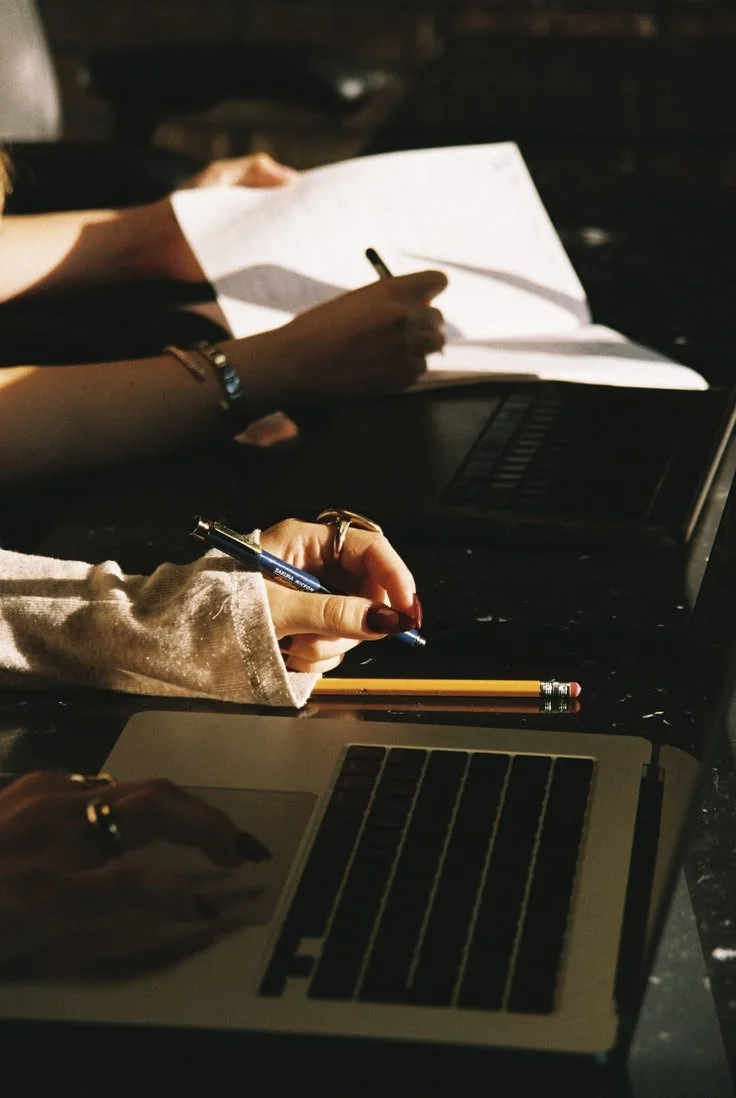 women's hand with red nail polish holds a pen whilst working on her laptop