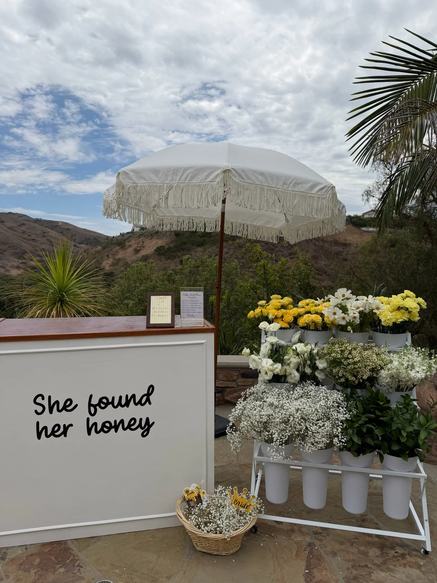 A bouquet making station with beautiful yellow and white flowers, a bar, and a white umbrella.