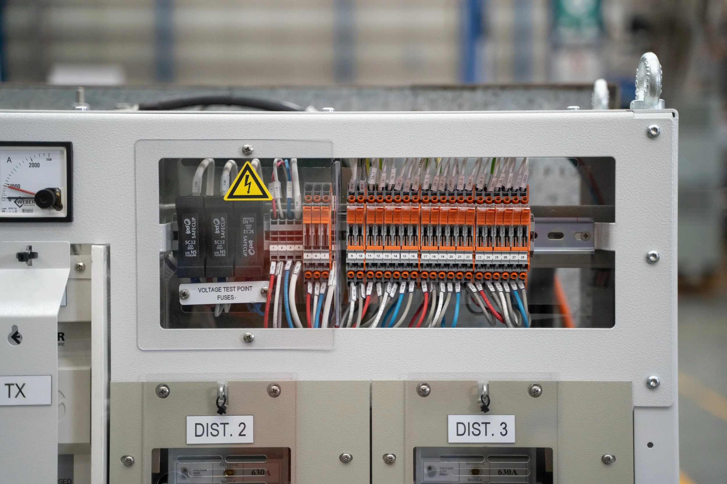 Electrical control panel with wiring, fuses, and warning labels in an industrial setting.