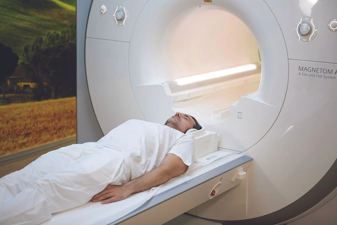 Mies makaa magneettikuvauslaitteen vuoteella, valmistautuen MRI-skannaukseen.