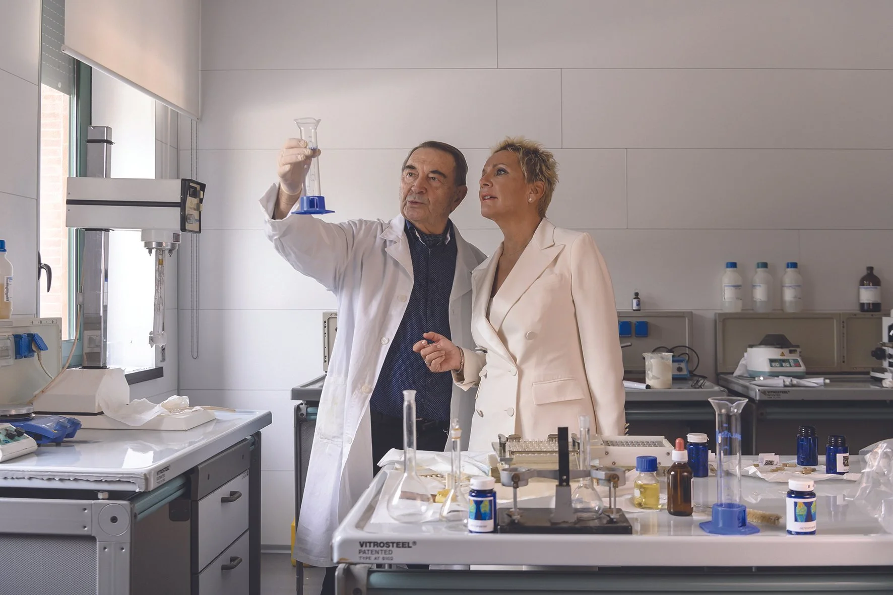 Kaksi laboranttia työskentelee laboratoriossa, toinen näyttää näytettä testiletkussa toisen katsoessa.