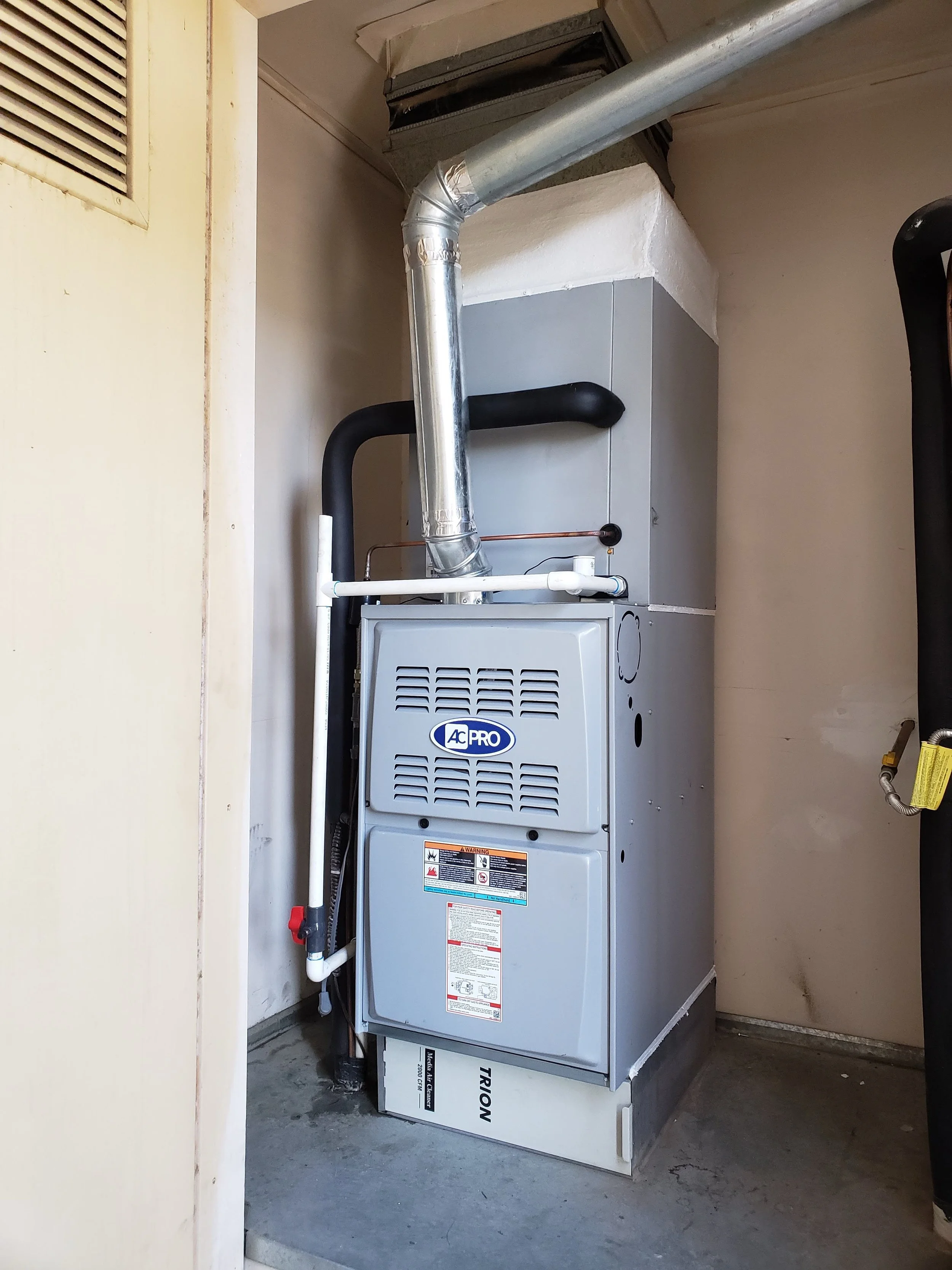 A central heating furnace in a utility room with ductwork and pipes connected to it, placed on a concrete floor.