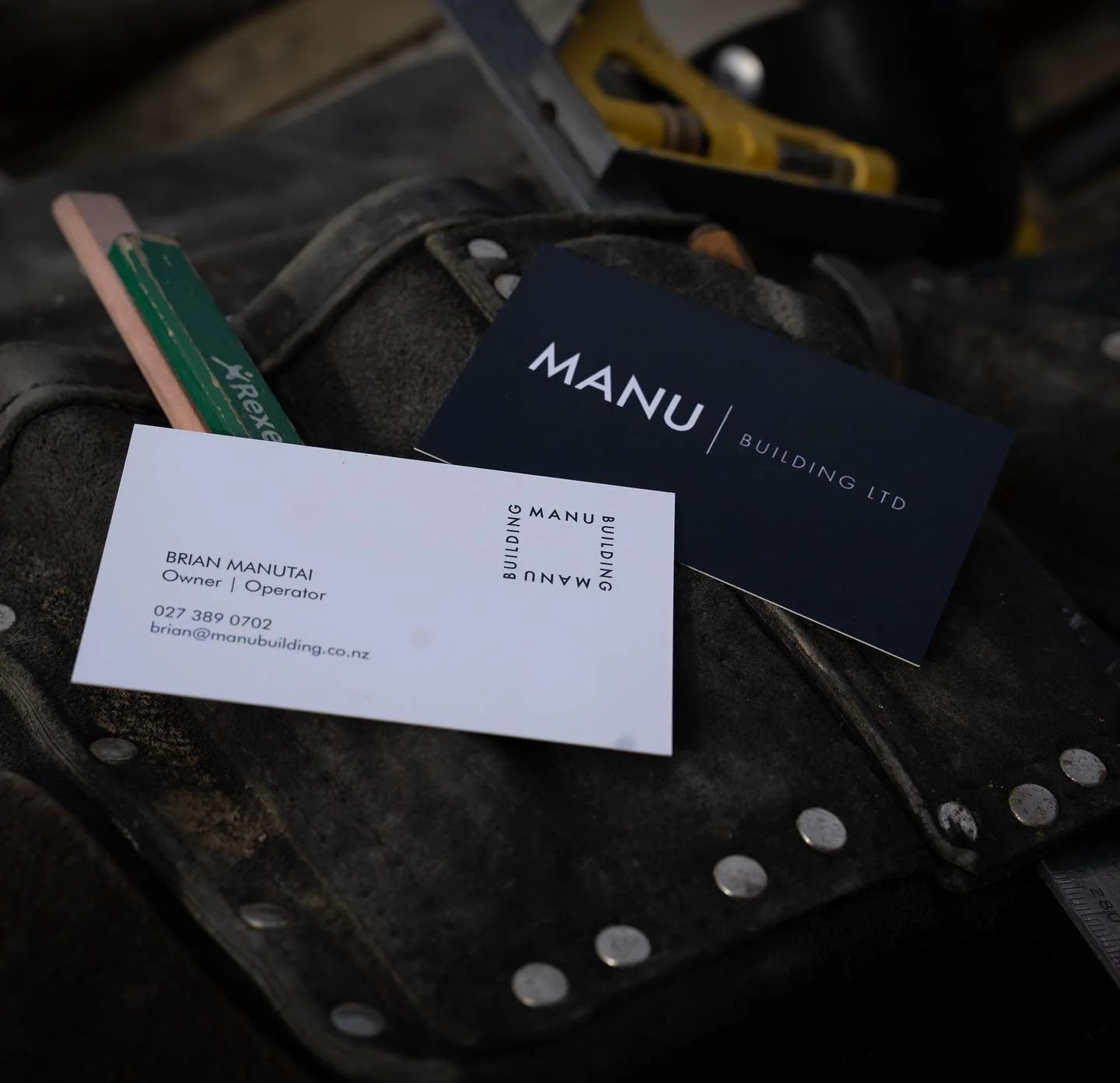 Business cards for MANU Building Ltd on a work ledge with construction tools.