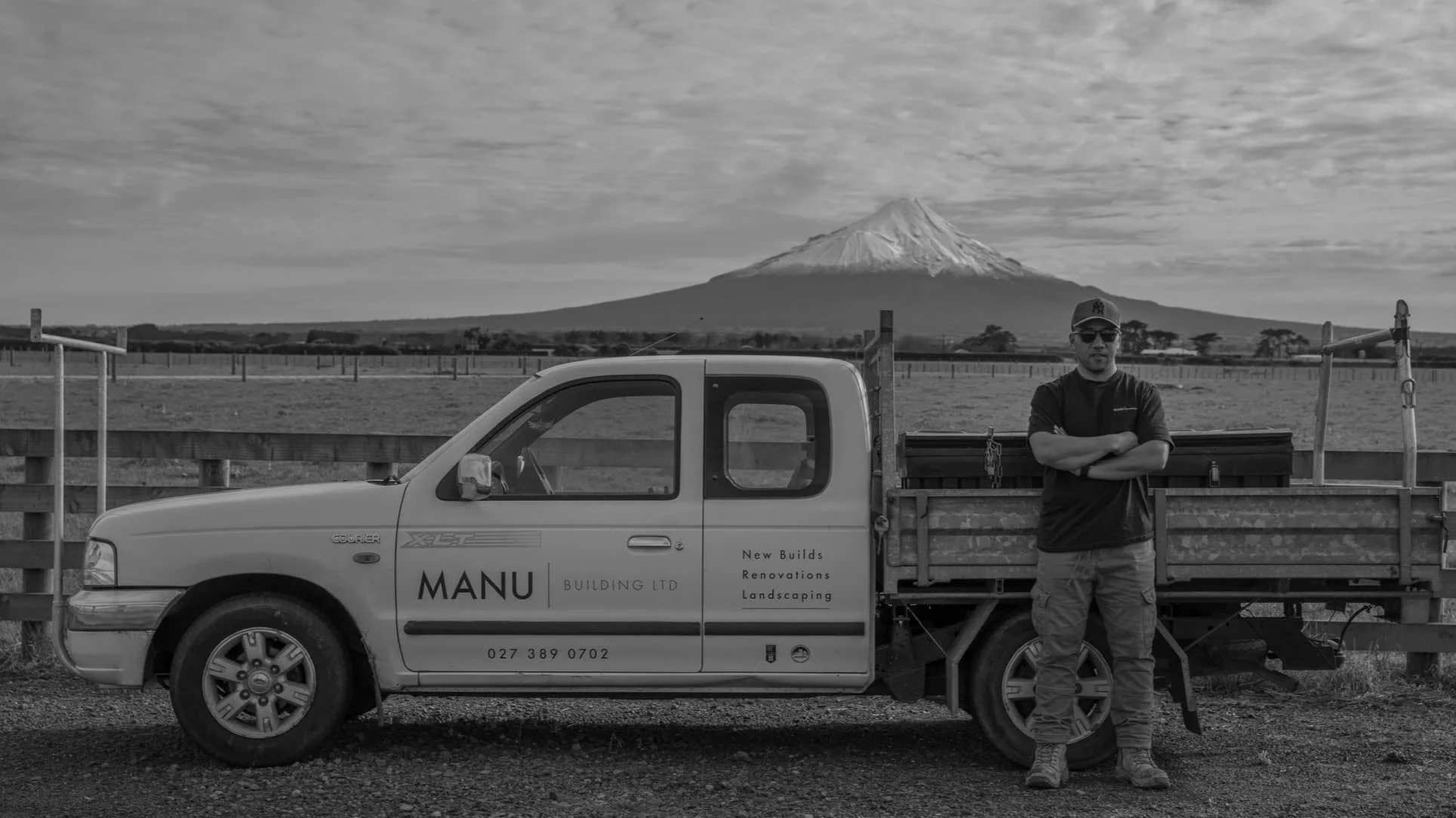 A man standing next to a small flatbed truck with Mount Taranaki in the background.