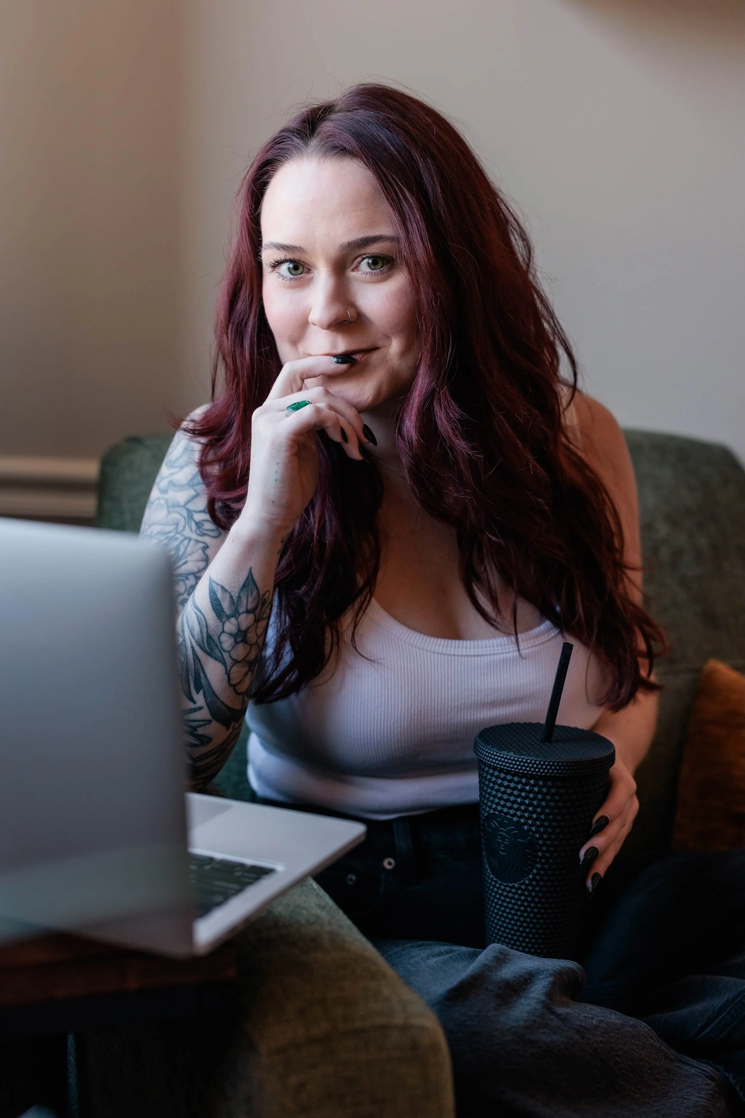 Kaylie sits in an armchair with a laptop and water cup.