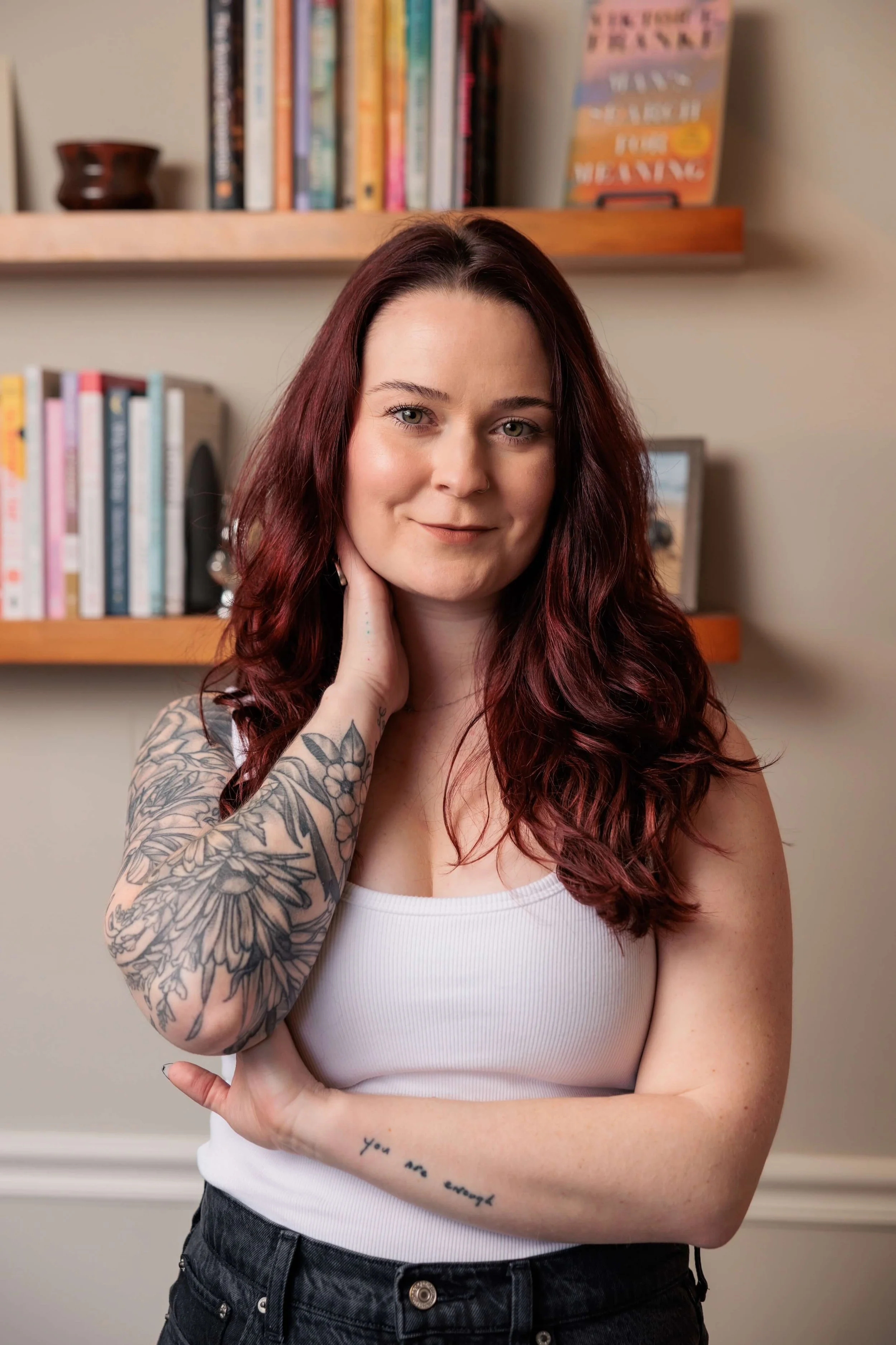 Kaylie stands before bookshelves in a white tank top.