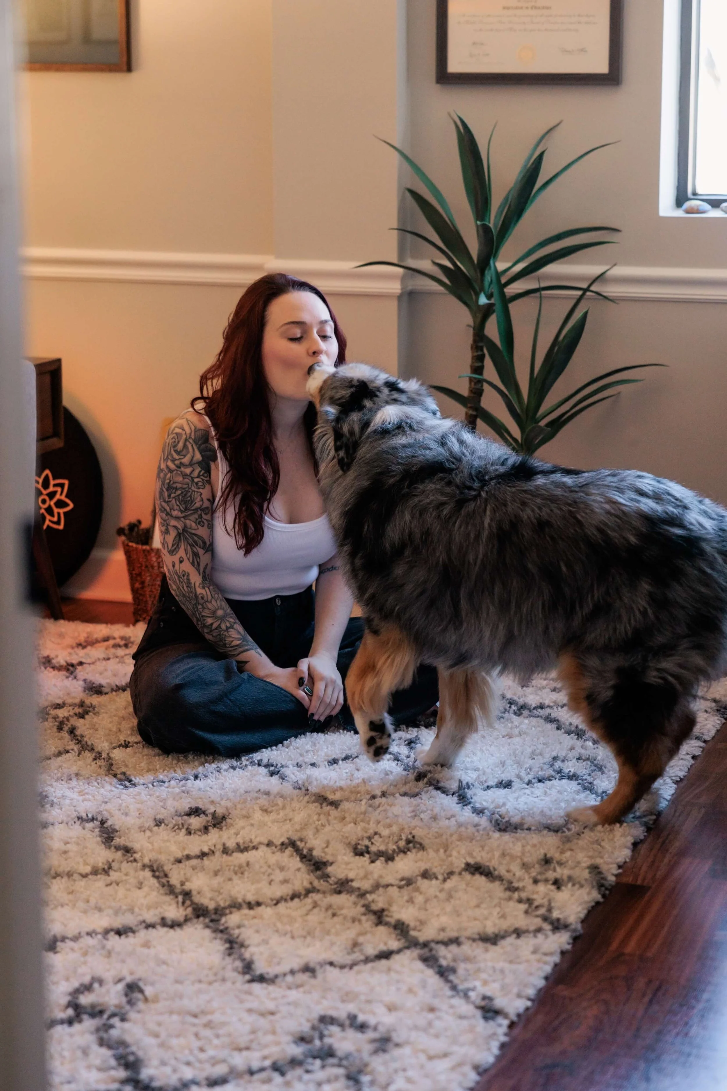 Kaylie sitting on the floor and kissing her Australian Shepherd