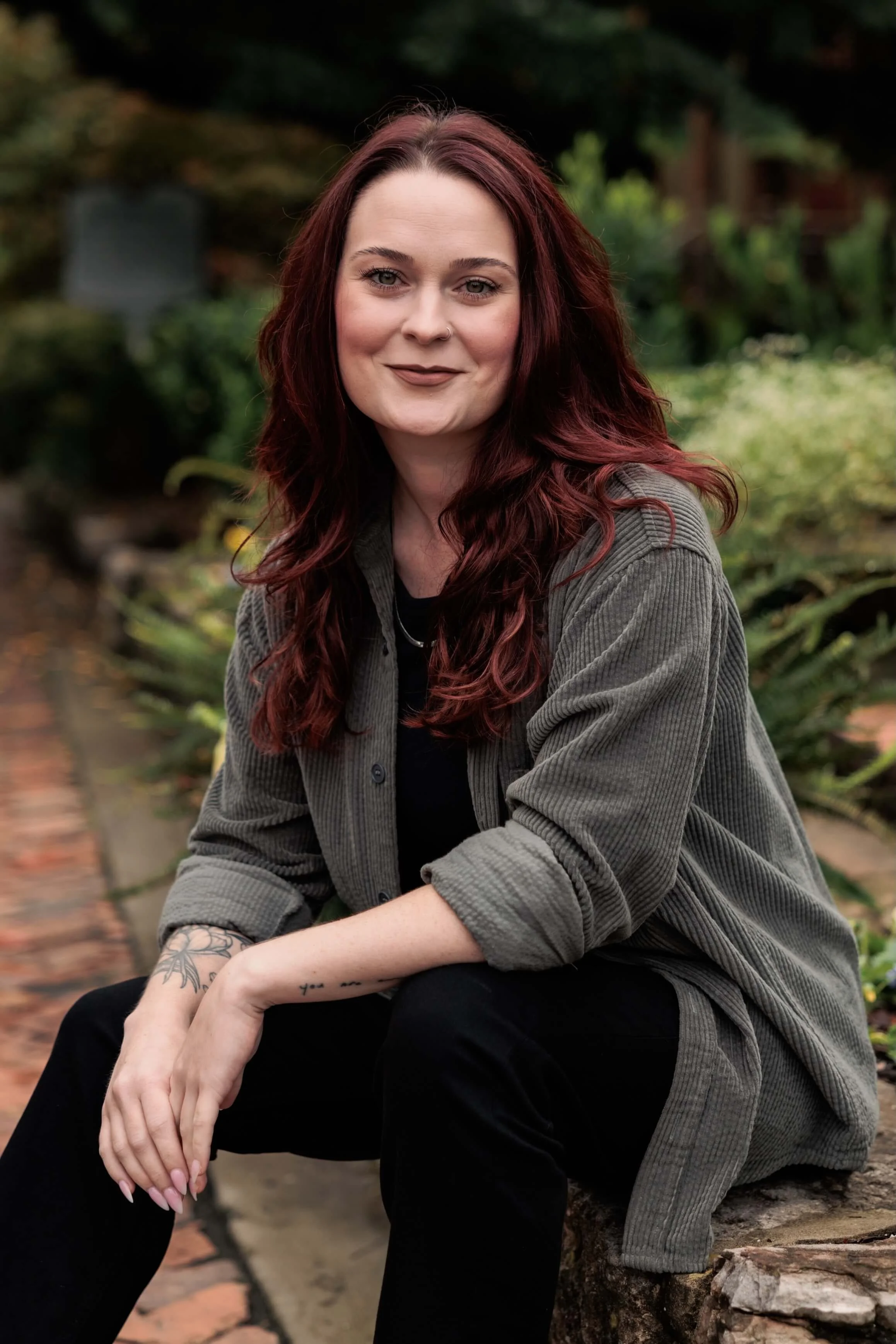 Kaylie sits outside in black pants and a gray overshirt.