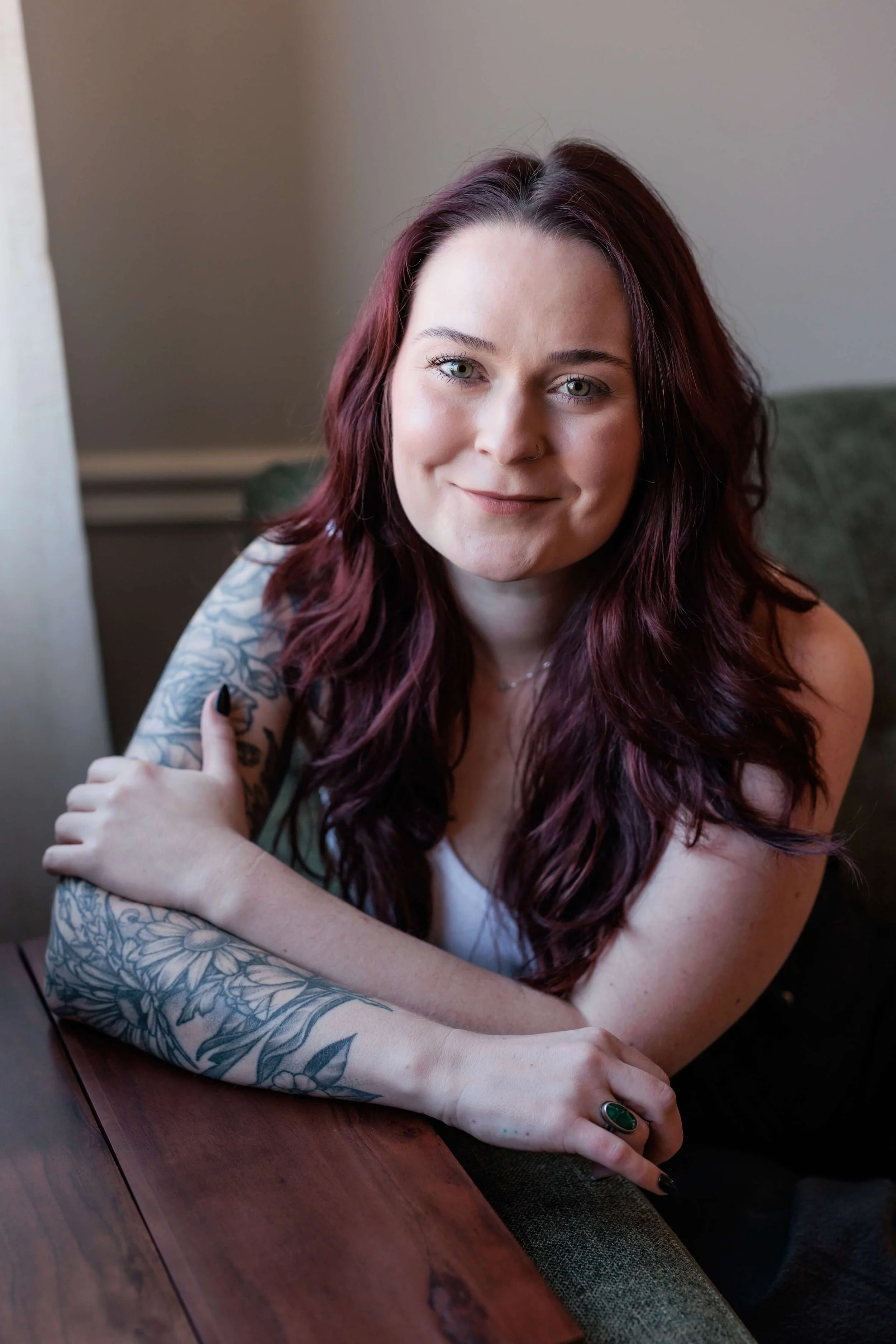 Kaylie leans over a desk, hugging her arm with a tattoo sleeve.
