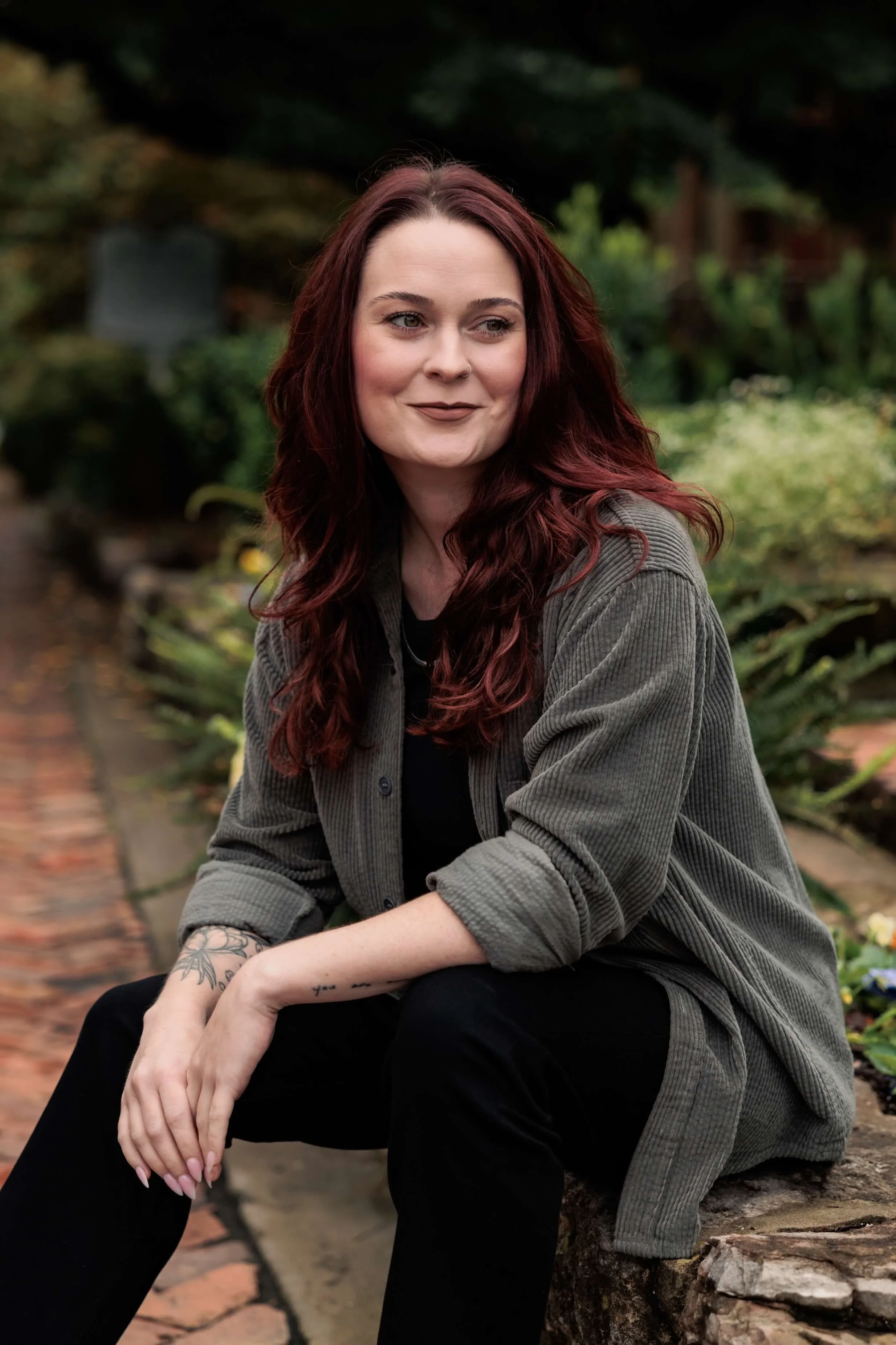 Kaylie sits outside in black pants and a gray overshirt.