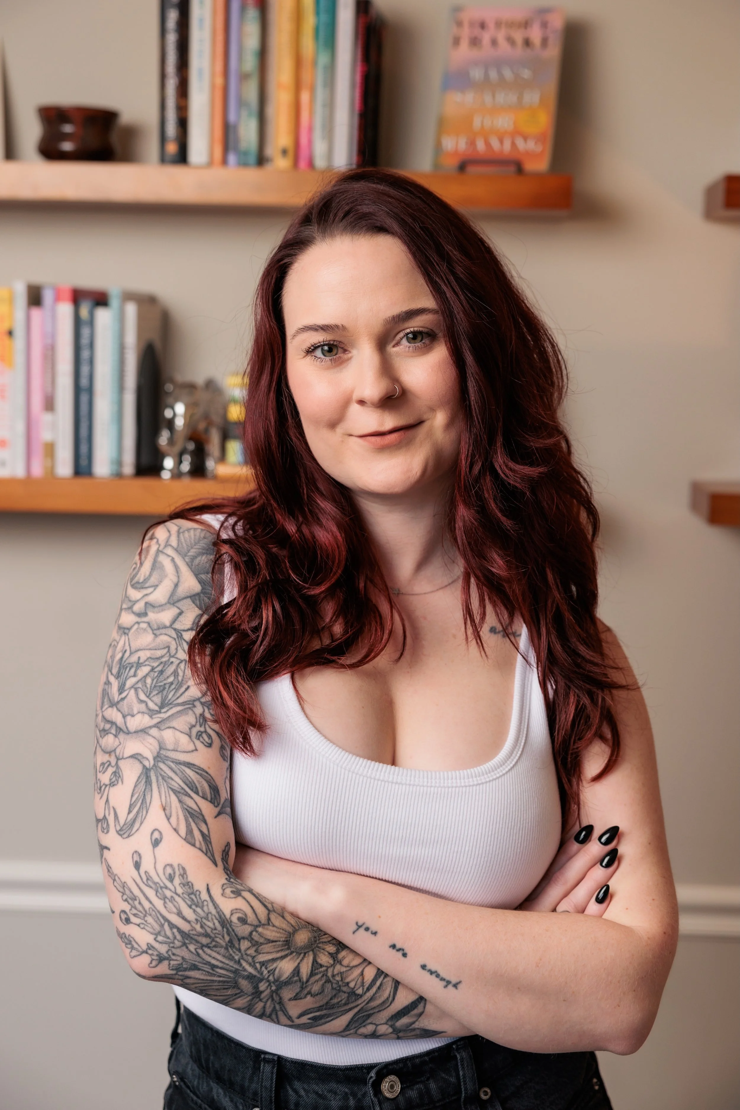 Kaylie stands before bookshelves in a white tank top.