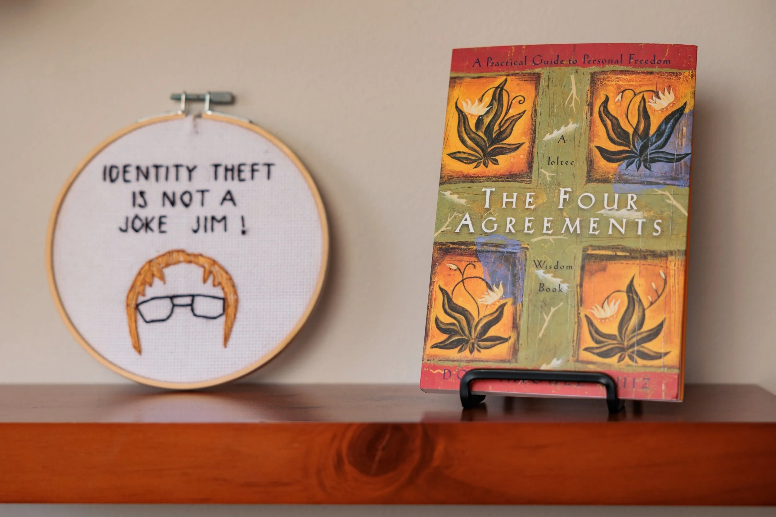 Embroidery round and a copy of The Four Agreements on a shelf.