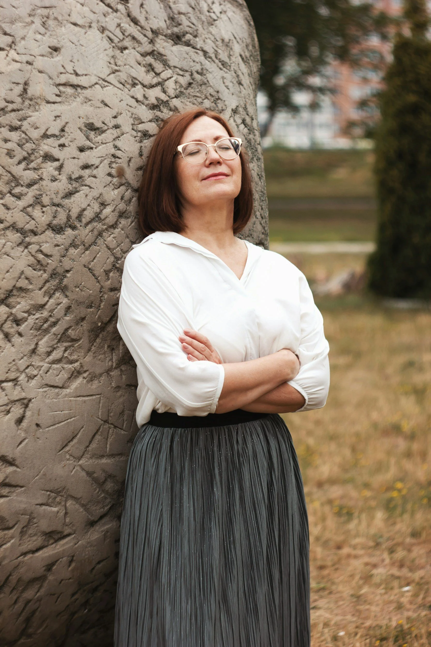 women with glasses leaning on a big grey rock