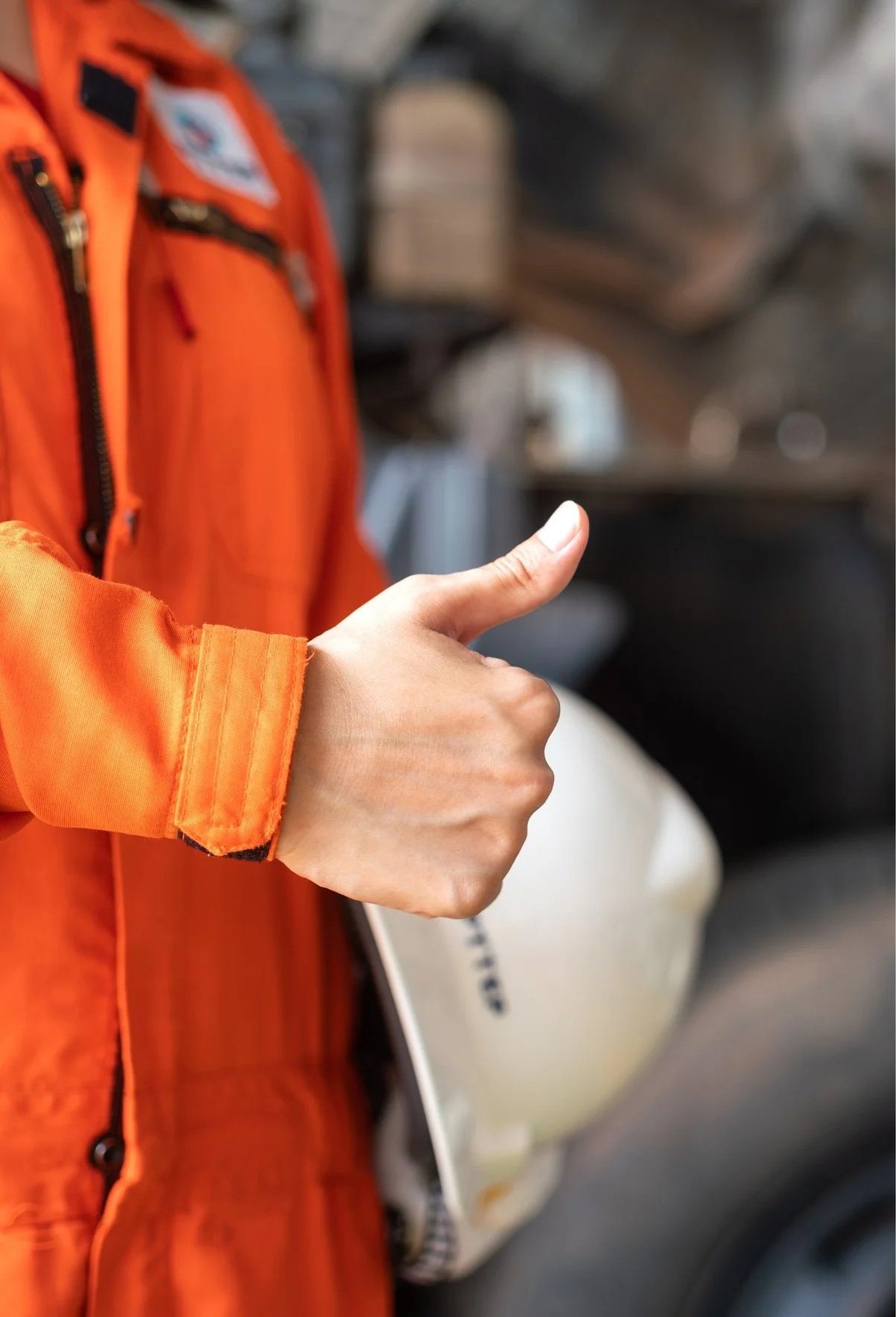 Person in an orange jacket giving a thumbs-up gesture, with a blurred background.