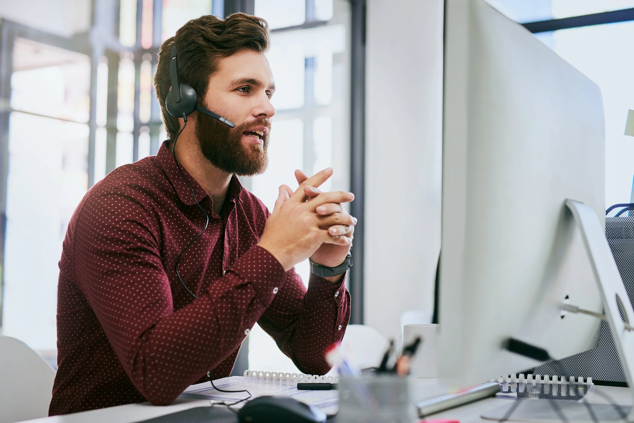 Relaxed man with headset in an office in front of his computer providing software support 