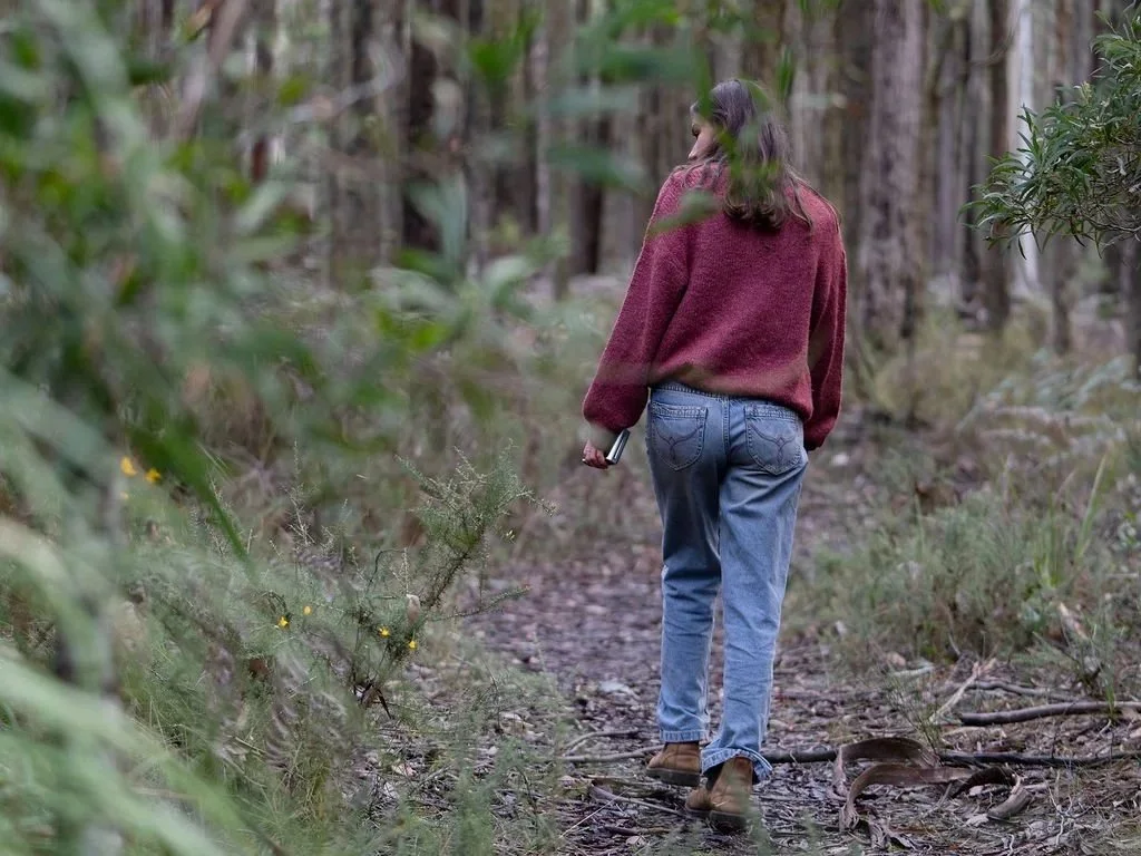 Young lady in forest, walking on track with jeans and jumper.