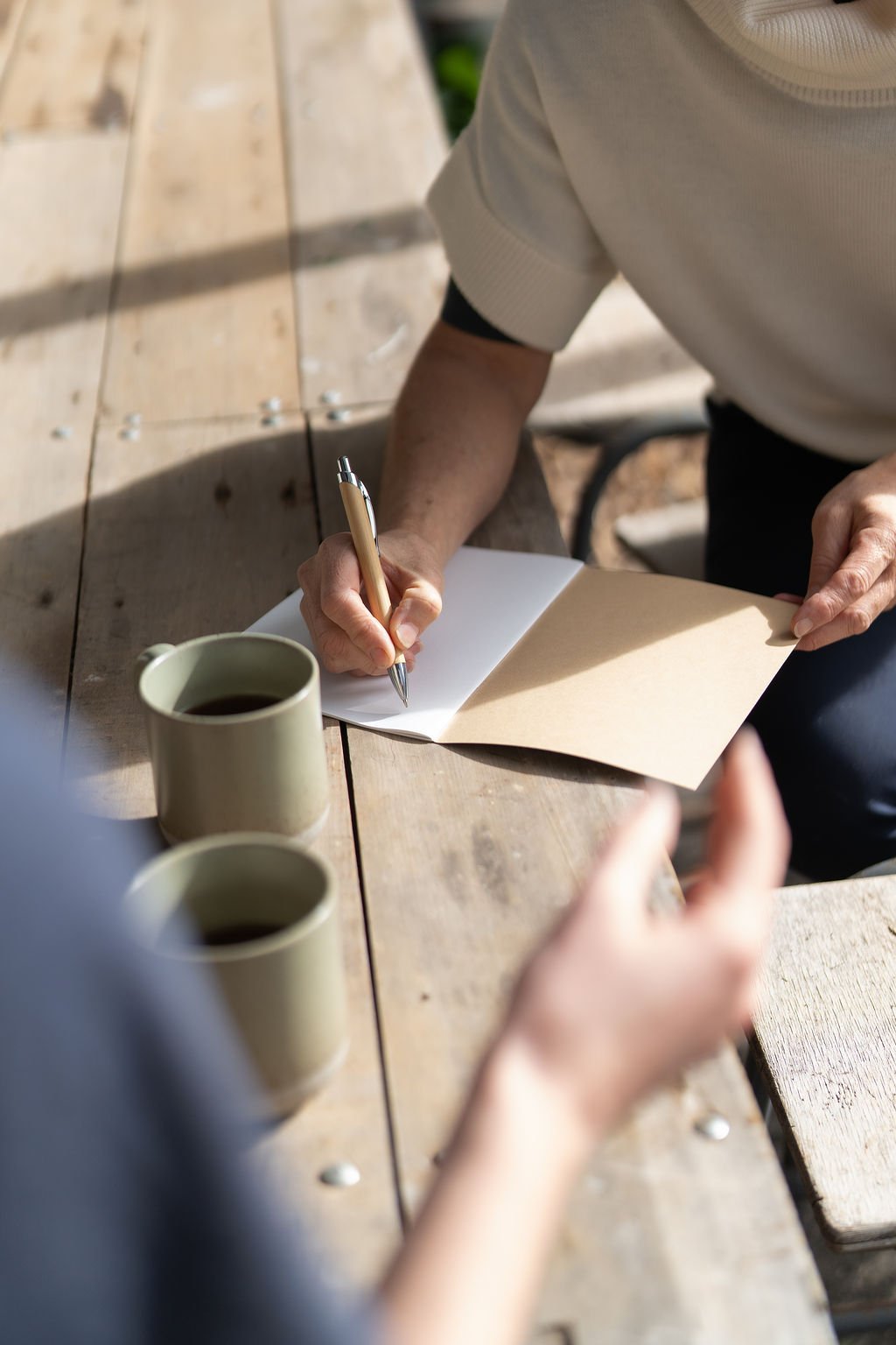 Person sitting at table writing in journal with cup of coffee.